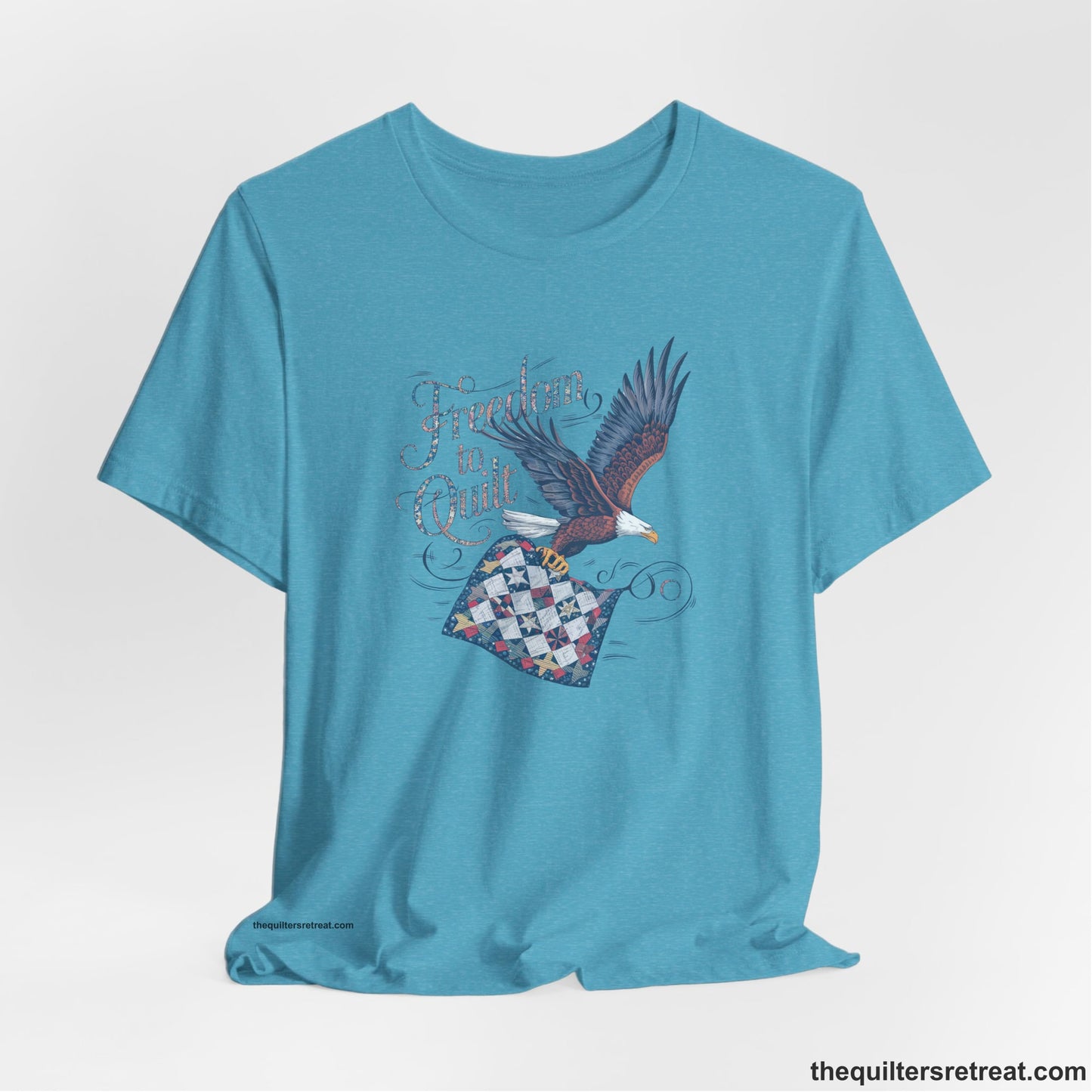 A Heather Aqua Short Sleeve T-Shirt with a freedom to quilt text with an eagle carrying a colorful patchwork quilt in vintage style