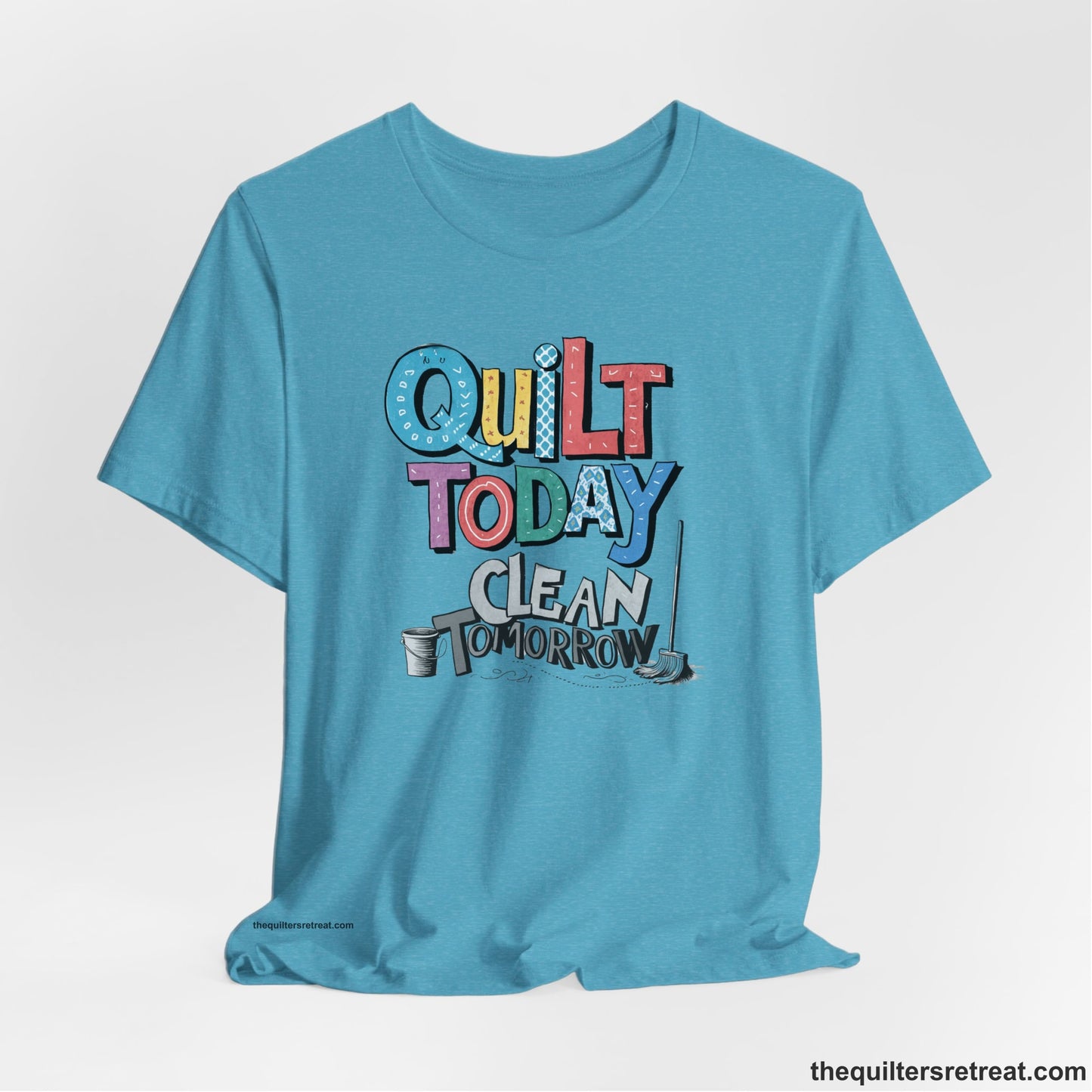 A Short Sleeve T-Shirt with a playful "Quilt Today Clean Tomorrow" text with colorful patterns and cleaning tools illustration