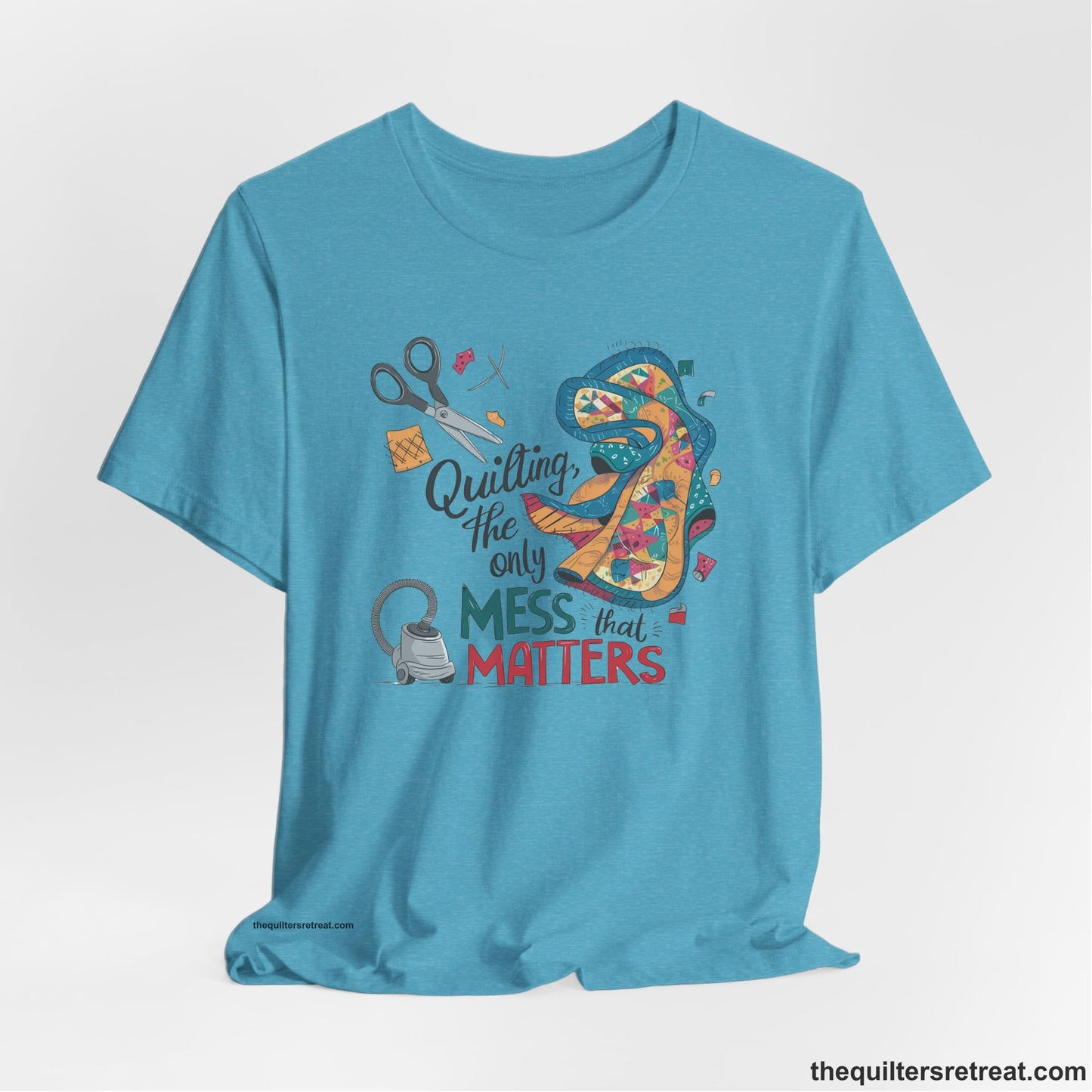 A Heather Aqua Short Sleeve T-Shirt with a quilting tools and patchwork pieces with bold "Quilting, the only mess that matters" text