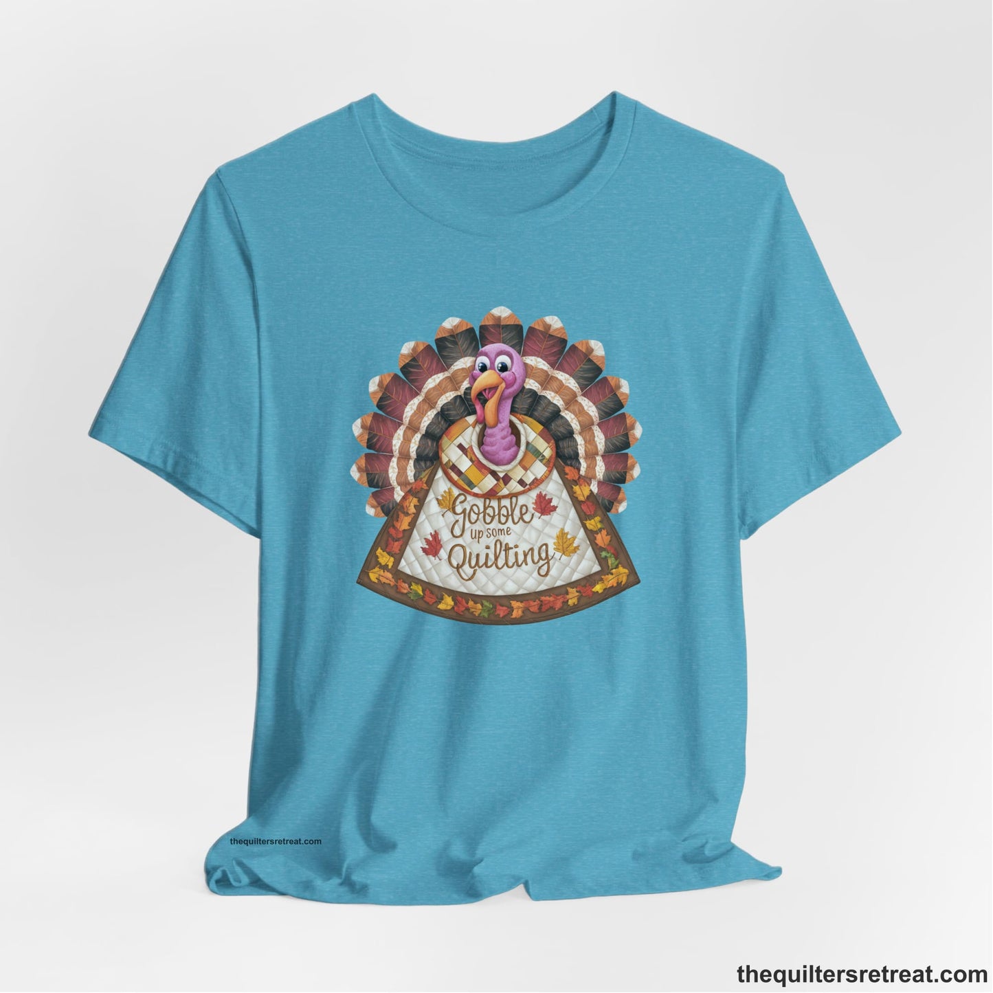 A Heather Aqua Short Sleeve T-Shirt with a colorful turkey with quilted feathers and "Gobble Up Some Quilting" text in a playful style
