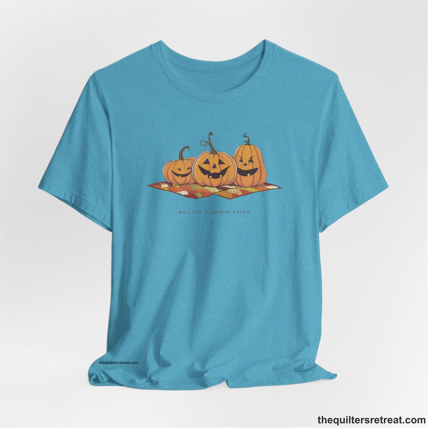 A Heather Aqua Short Sleeve T-Shirt with a playful jack-o'-lantern trio on a quilt with "Quilted Pumpkin Patch" text