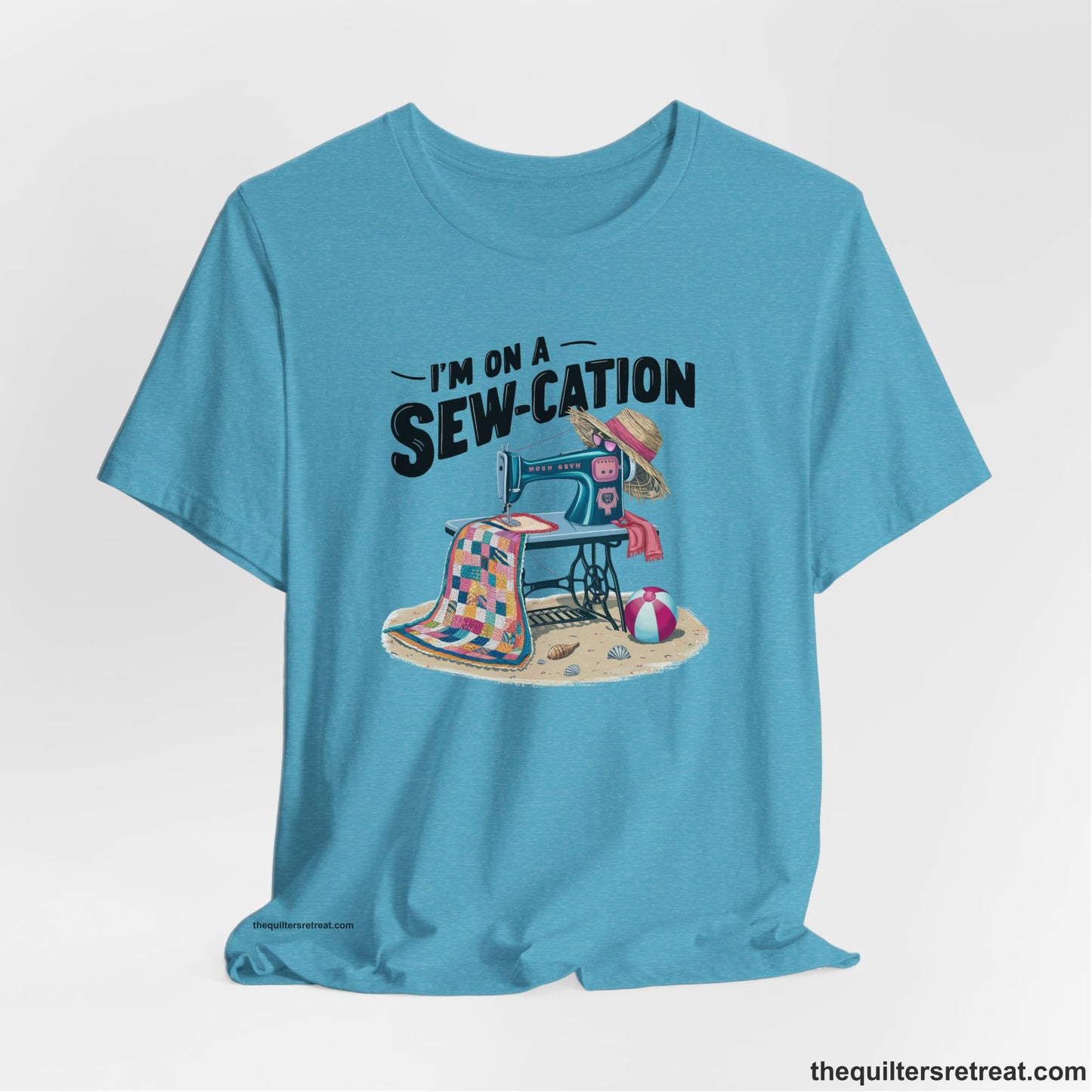 A Heather Aqua Short Sleeve T-Shirt with a vintage sewing machine with colorful quilt, beach items, and "I'm On A Sew-Cation" text