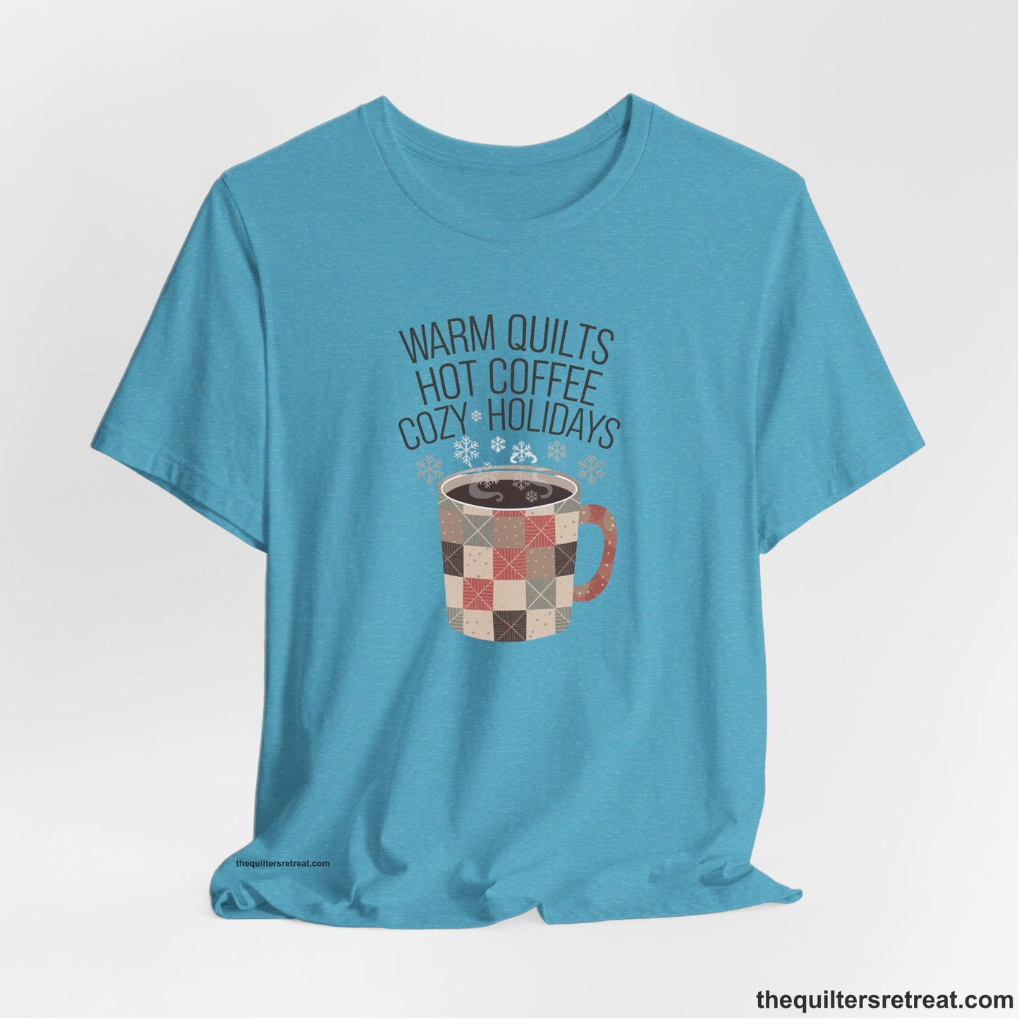 A Heather Aqua Short Sleeve T-Shirt with a warm quilts hot coffee cozy holidays text with a patchwork mug and snowflakes