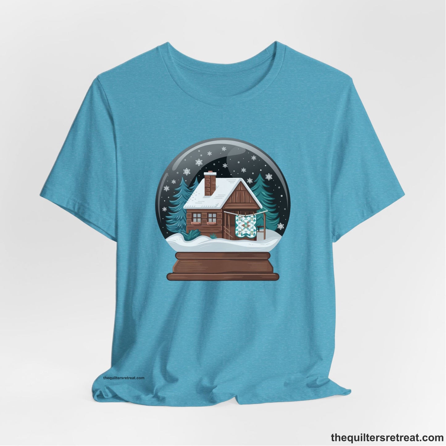 A Heather Aqua Short Sleeve T-Shirt with a cabin in a snow globe with snowflakes and trees, in a cozy rustic style