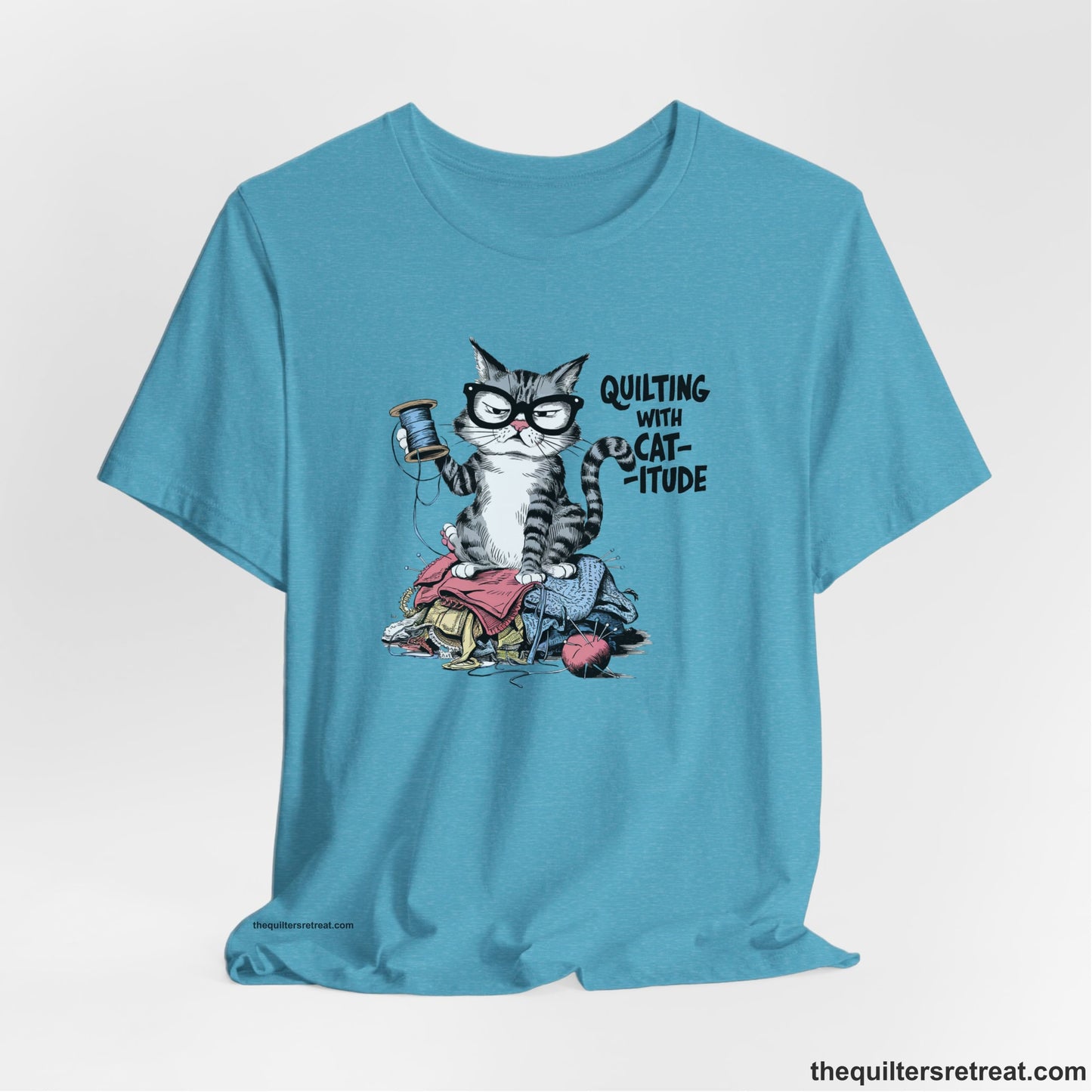A Heather Aqua Short Sleeve T-Shirt with a grumpy cat holding thread spool atop fabric pile with "Quilting with Cat-itude" text