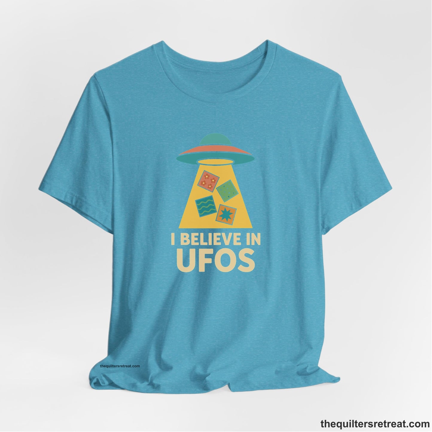 A Heather Aqua Short Sleeve T-Shirt with a colorful UFO with quilt patterns and bold "I Believe in UFOs" text in retro style
