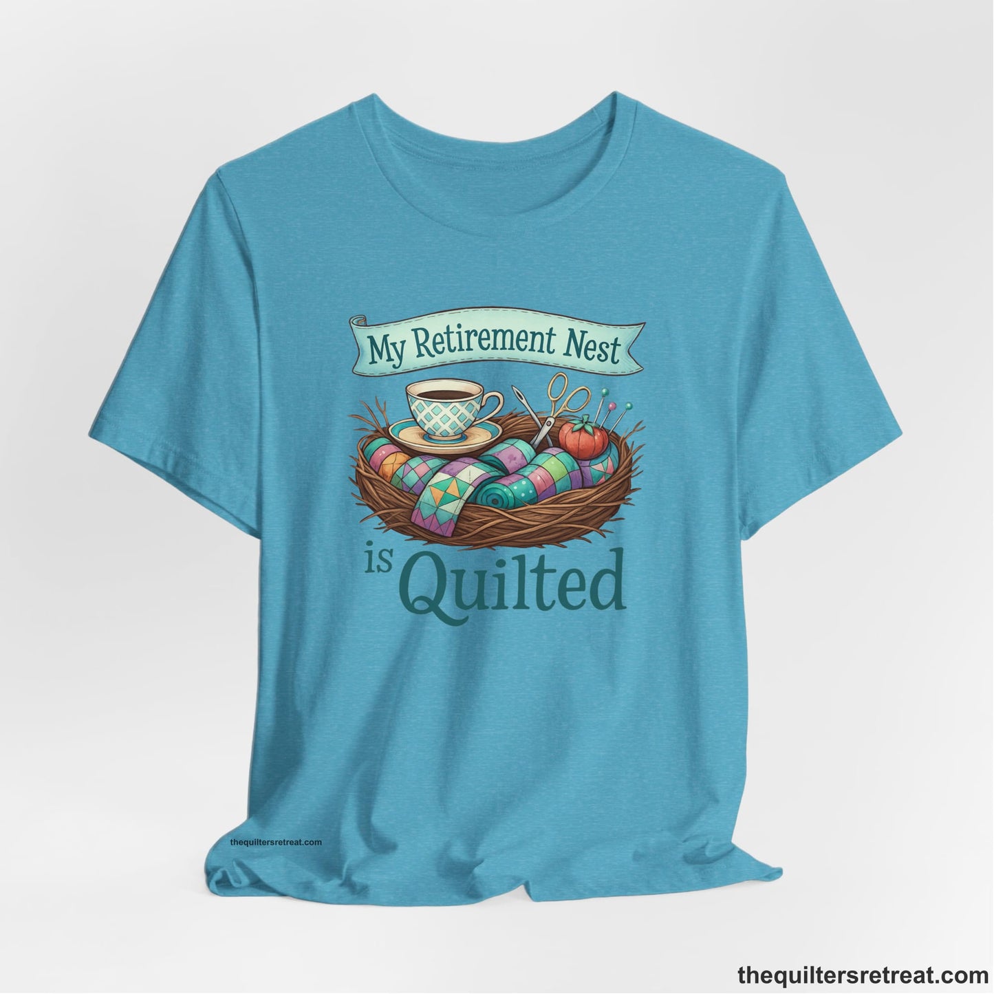 A Heather Aqua Short Sleeve T-Shirt with a My Retirement Nest is Quilted text with a cozy sewing elements illustration