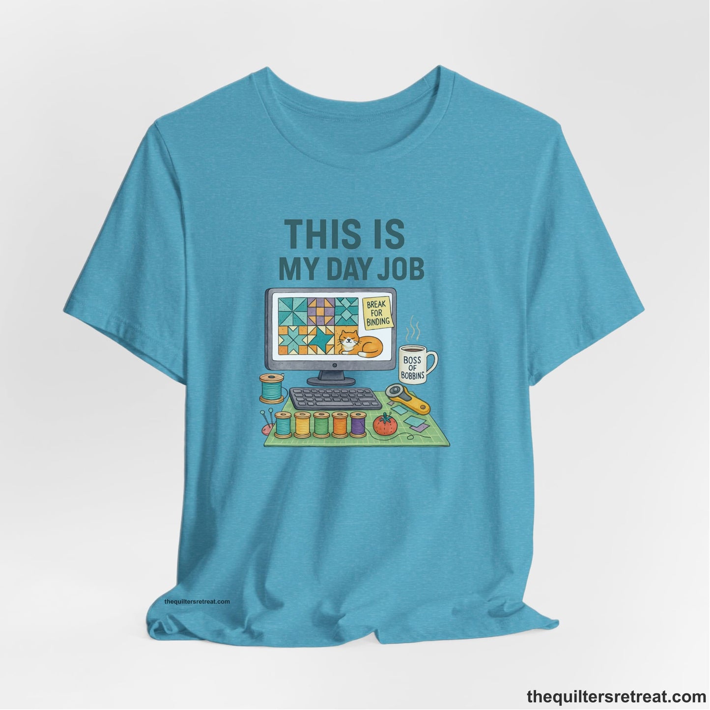 A Heather Aqua Short Sleeve T-Shirt with a computer quilt design, cat illustration, "THIS IS MY DAY JOB" text with sewing tools, playful style