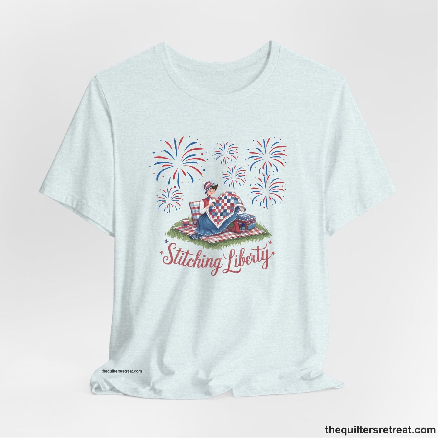 A Heather Ice Blue Short Sleeve T-Shirt with a vintage illustration of woman quilting with fireworks and "Stitching Liberty" text in patriotic style
