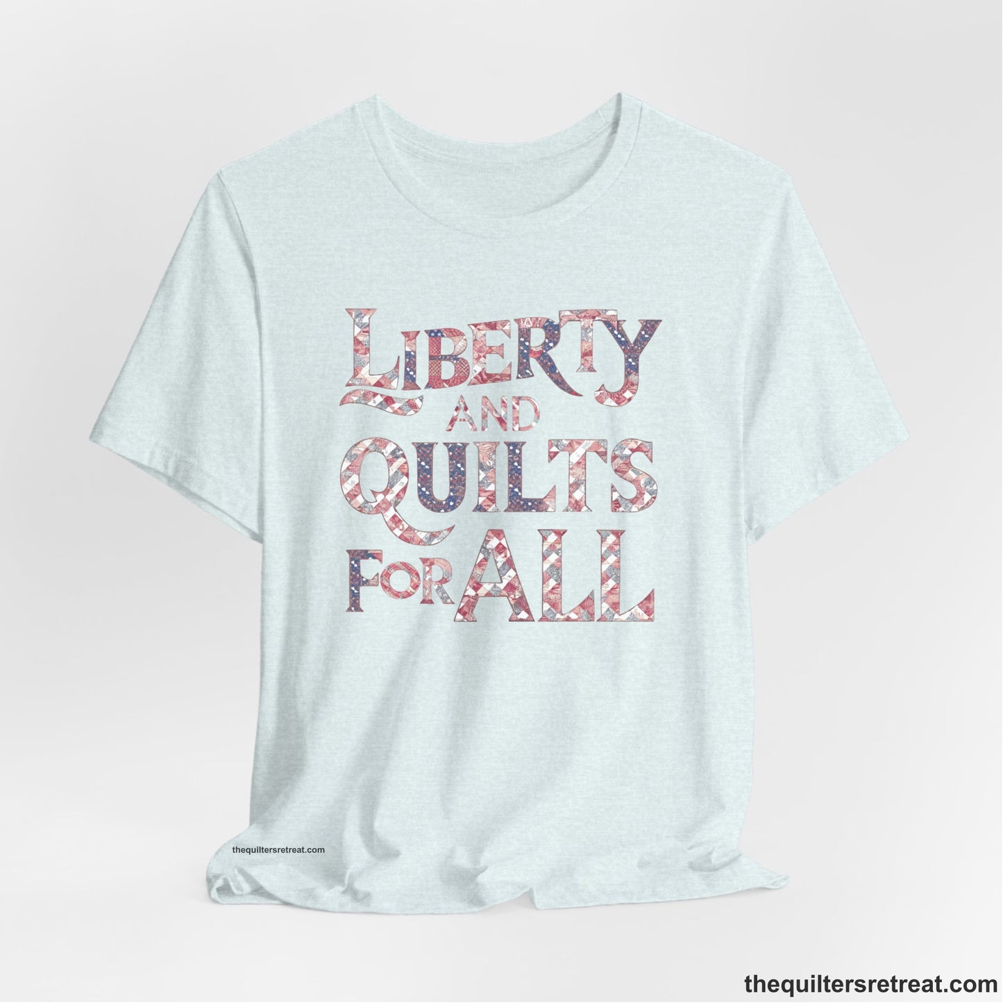 A Heather Ice Blue Short Sleeve T-Shirt with a Liberty and Quilts for All" text with patchwork quilt pattern in a vintage style