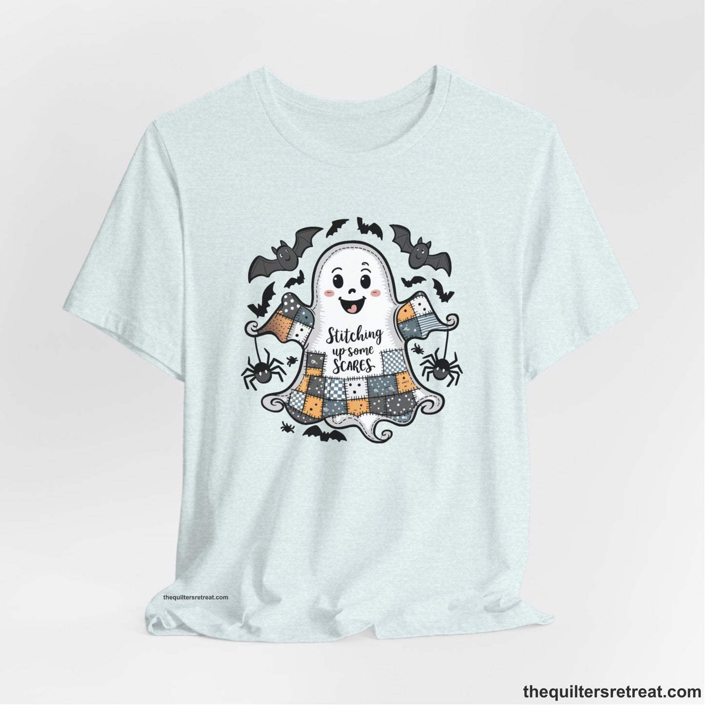 A Heather Ice Blue Short Sleeve T-Shirt with a cute patchwork ghost with "Stitching up some Scares" text and playful bats in a whimsical style