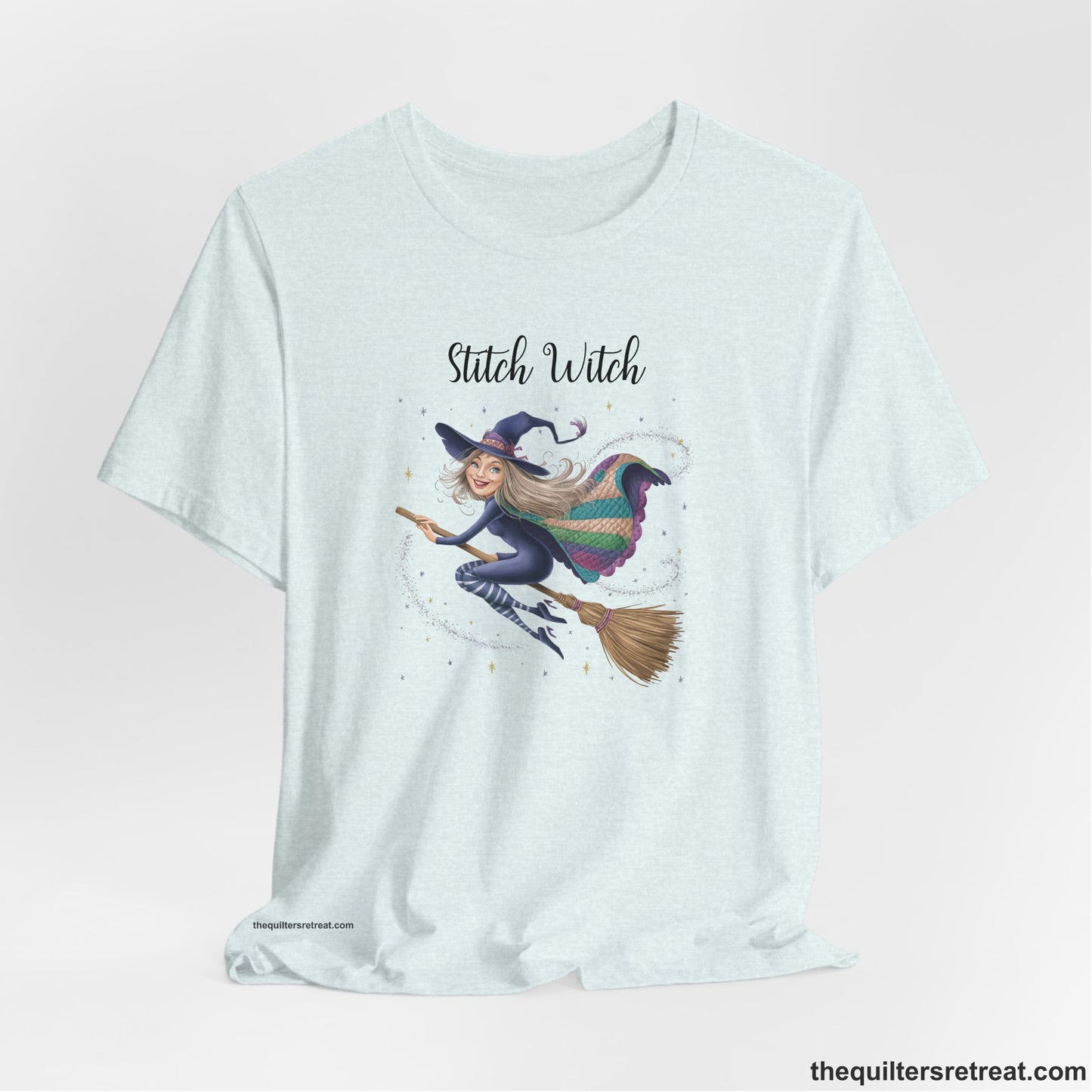 A Heather Ice Blue Short Sleeve T-Shirt with a playful witch on broomstick with patchwork cape and starry background in a whimsical style