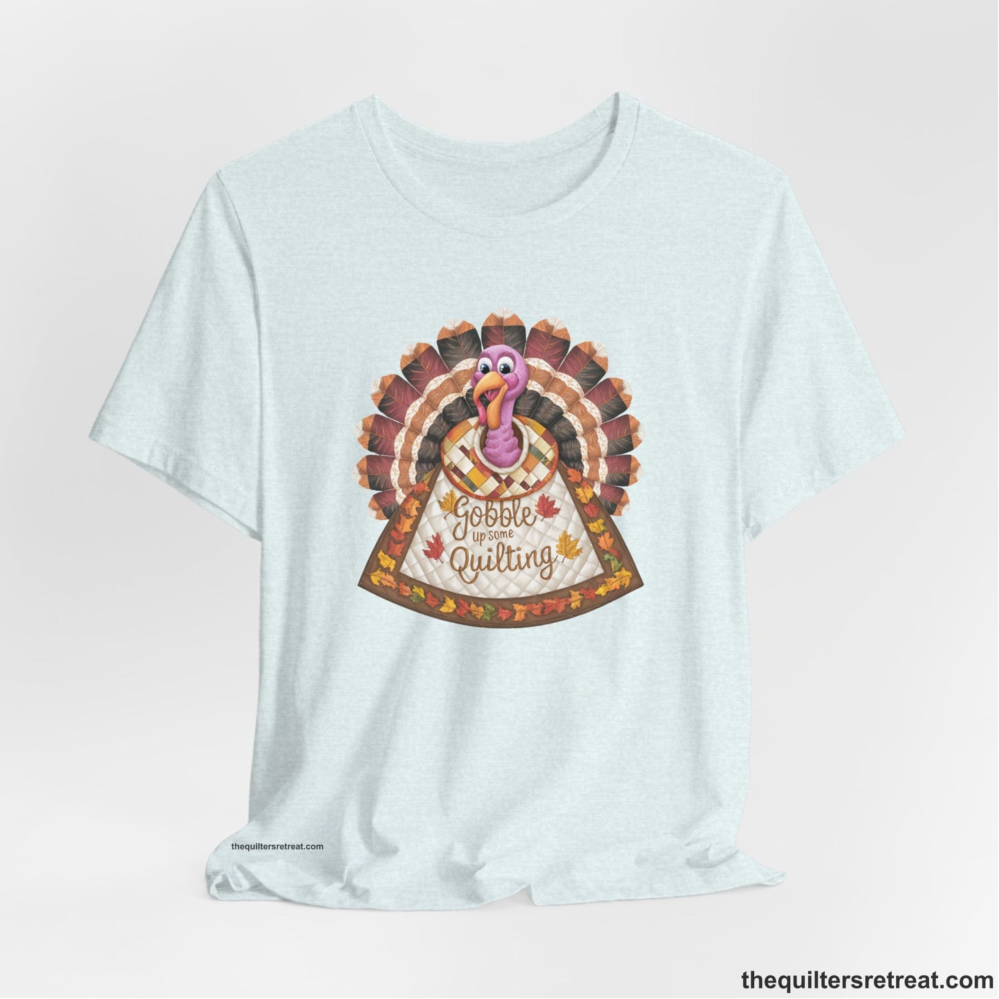 A Heather Ice Blue Short Sleeve T-Shirt with a colorful turkey with quilted feathers and "Gobble Up Some Quilting" text in a playful style