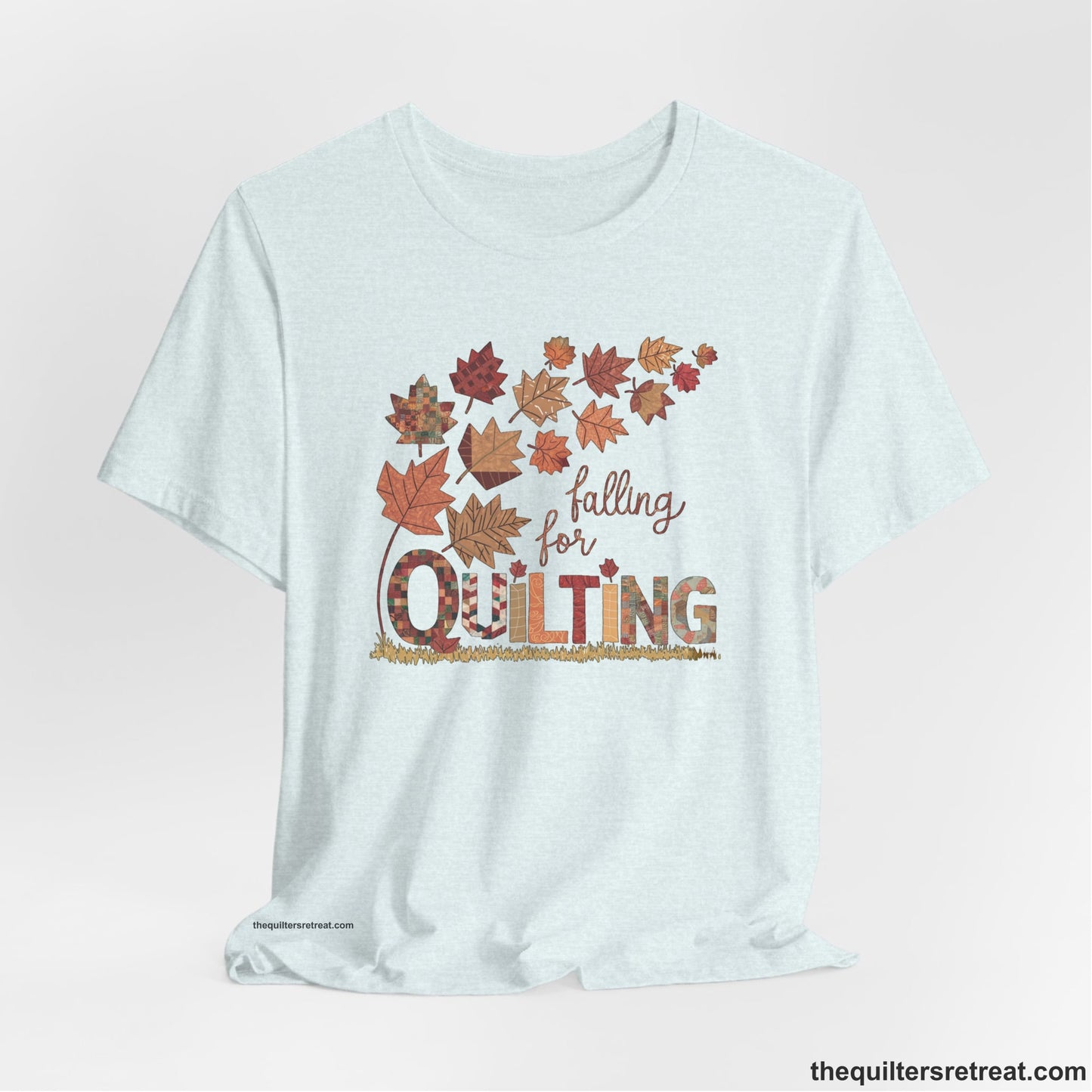 A Heather Ice Blue Short Sleeve T-Shirt with a falling autumn leaves and "Falling for Quilting" text in a patchwork style