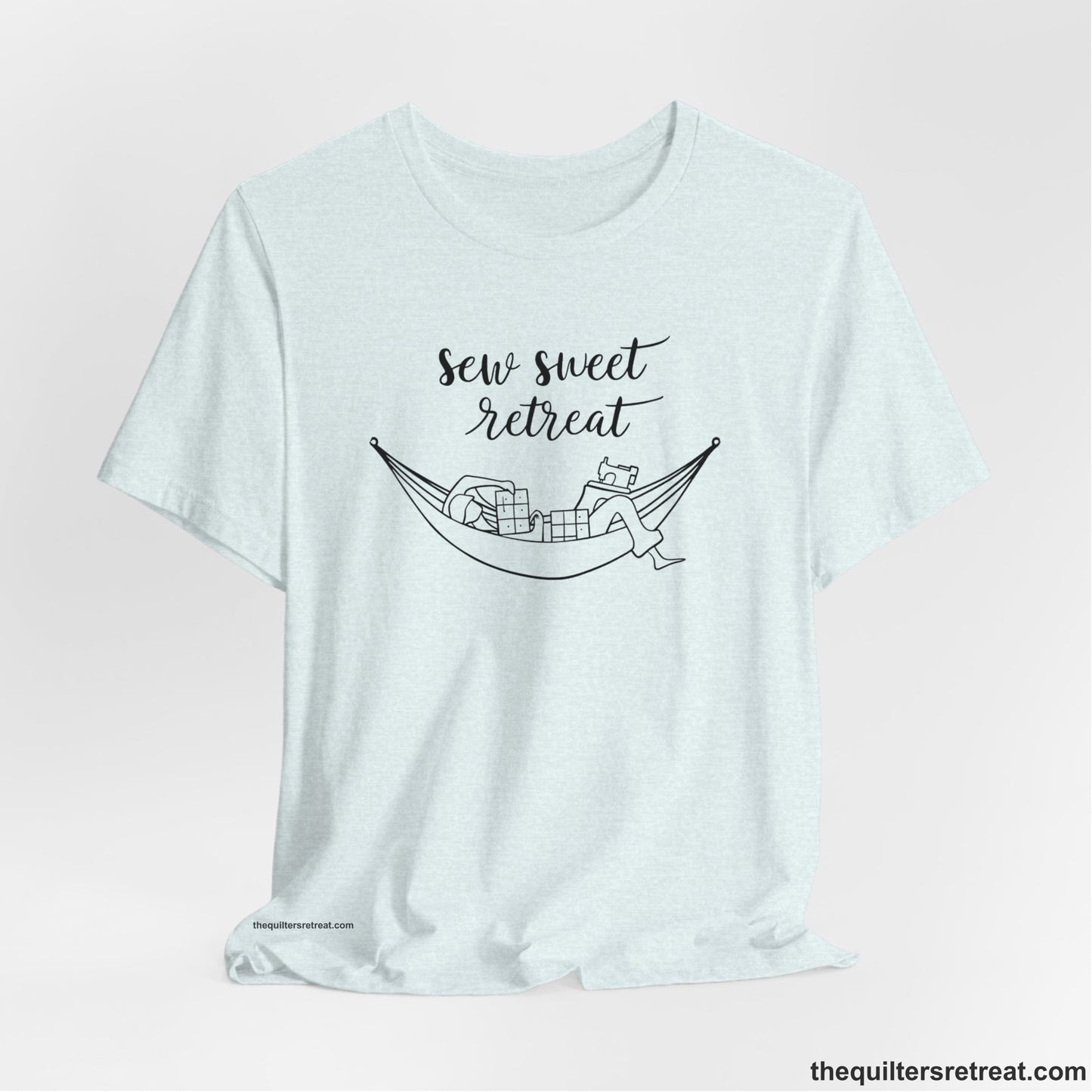 A Heather Ice Blue Short Sleeve T-Shirt with a sewing machine and thread spools with "Sew Sweet Retreat" in whimsical script