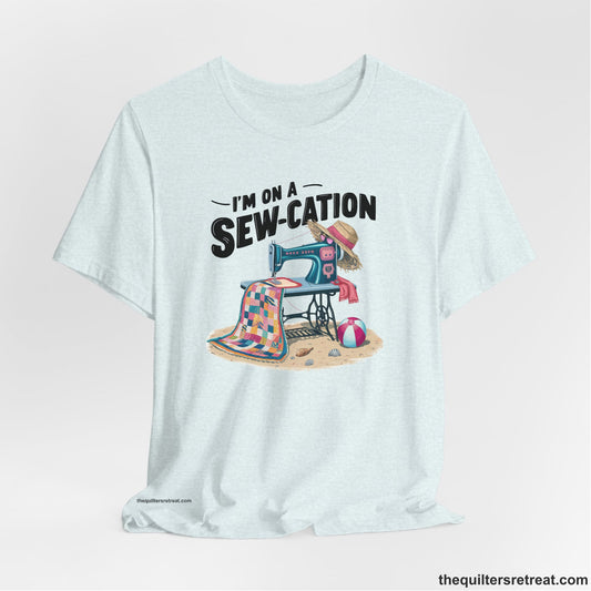 A Heather Ice Blue Short Sleeve T-Shirt with a vintage sewing machine with colorful quilt, beach items, and "I'm On A Sew-Cation" text