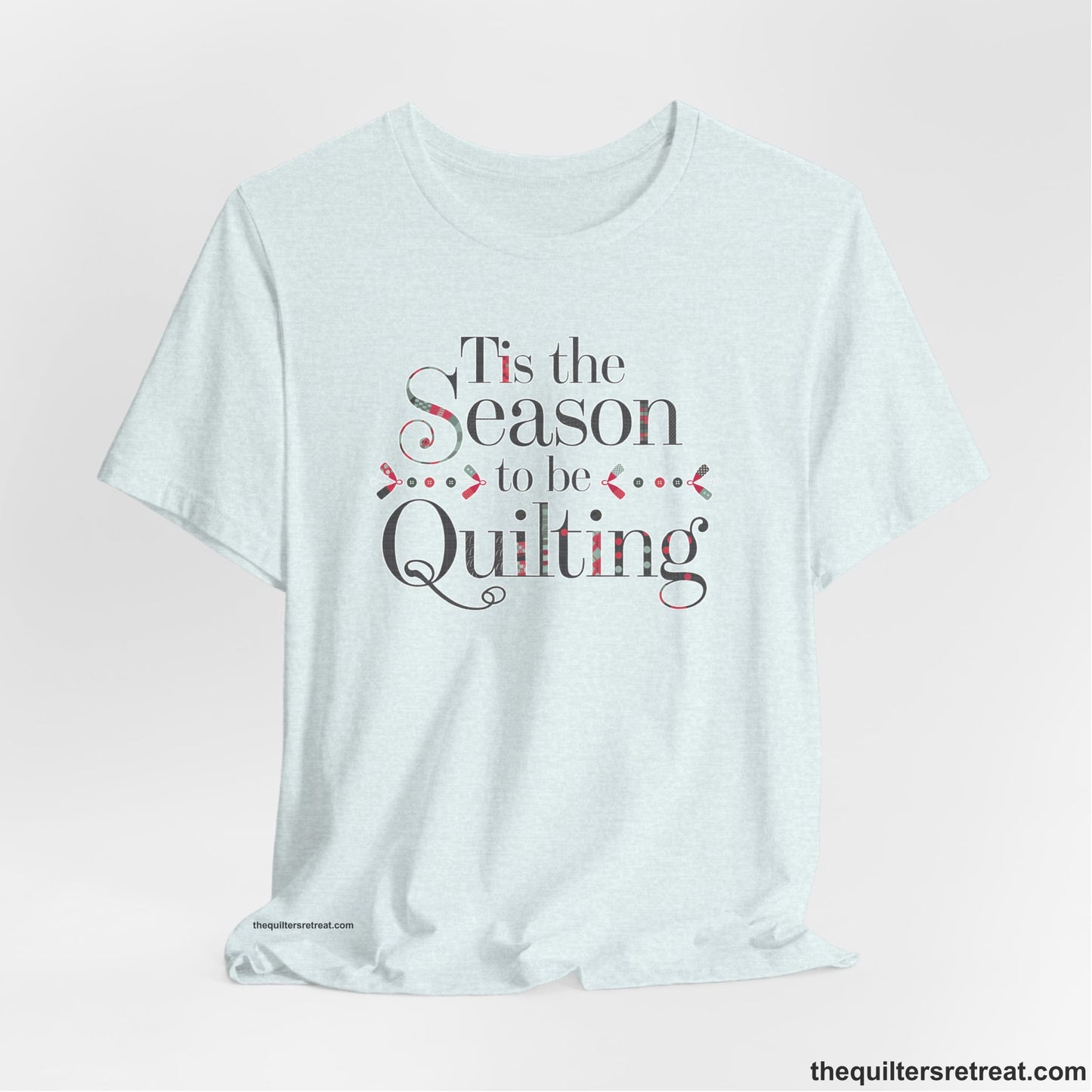 A Heather Ice Blue Short Sleeve T-Shirt with a tis the season to be quilting text with festive patchwork pattern in a cheerful style