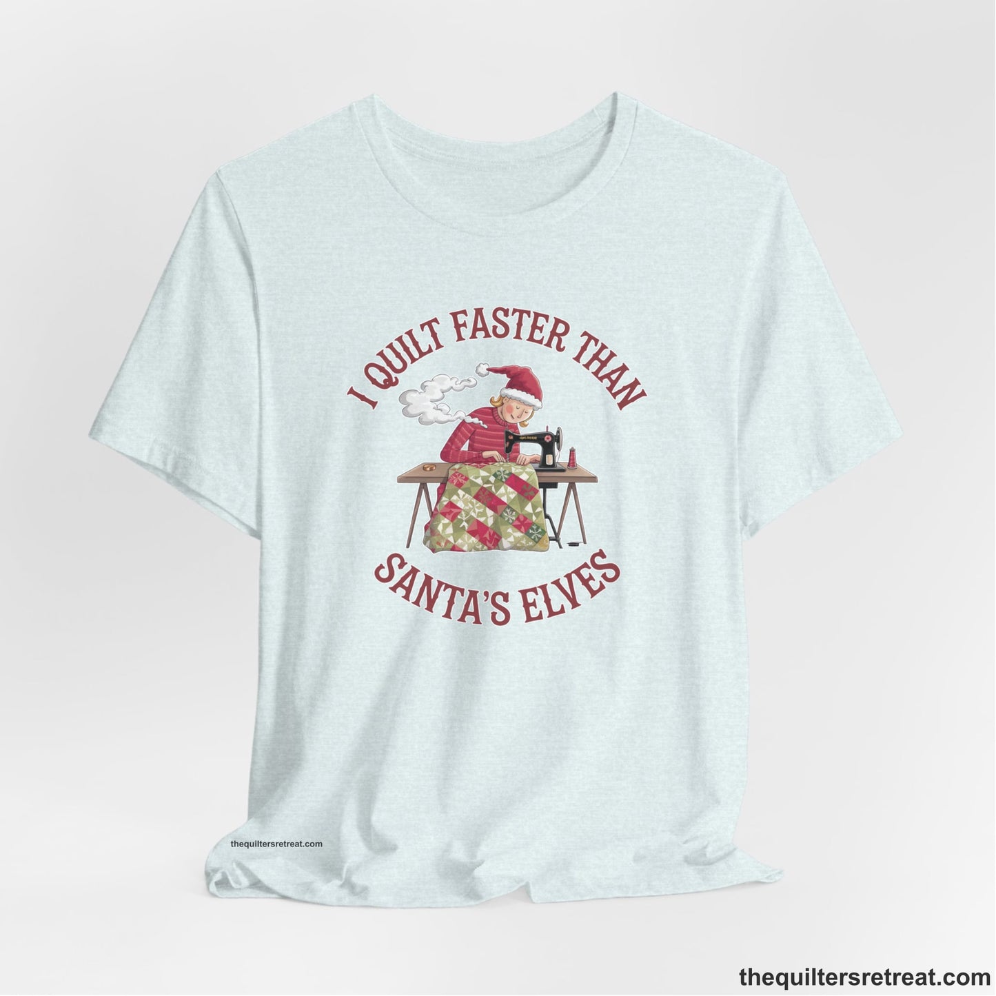 A Heather Ice Blue Short Sleeve T-Shirt with a whimsical illustration of a quilting woman with "I Quilt Faster Than Santa's Elves" text