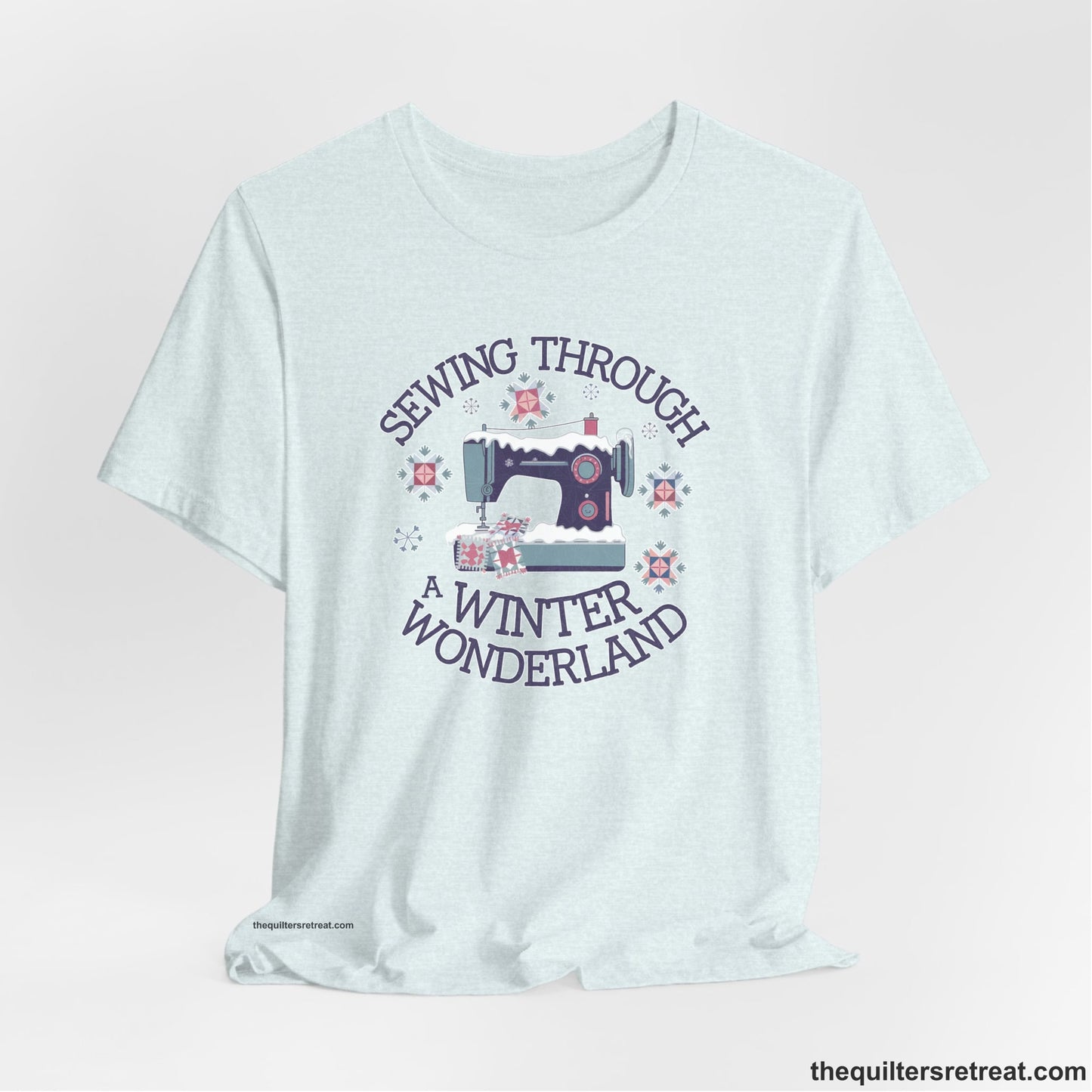 A Heather Ice Blue Short Sleeve T-Shirt with a sewing machine covered in snow with festive quilting elements and "Sewing Through a Winter Wonderland" text
