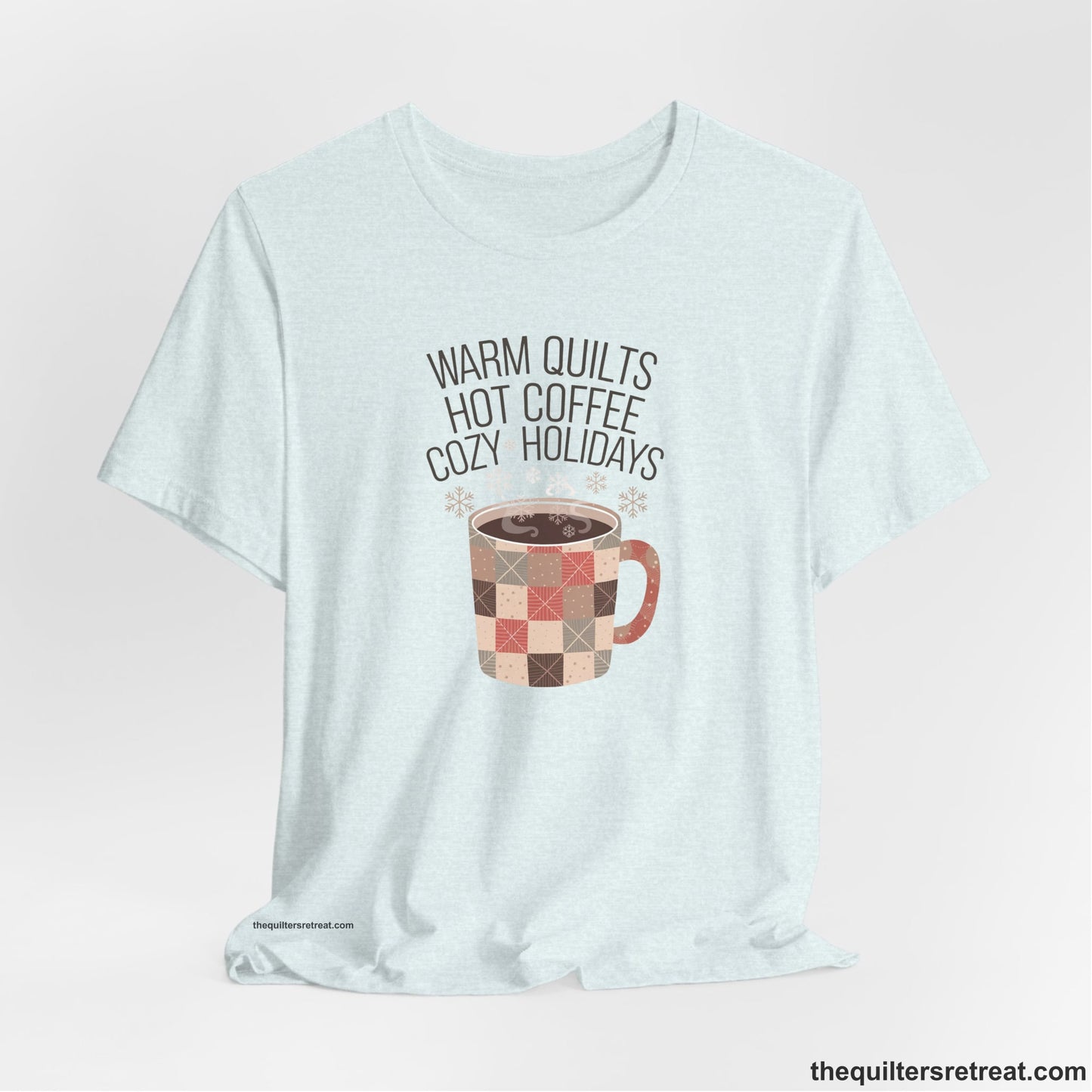 A Heather Ice Blue Short Sleeve T-Shirt with a warm quilts hot coffee cozy holidays text with a patchwork mug and snowflakes