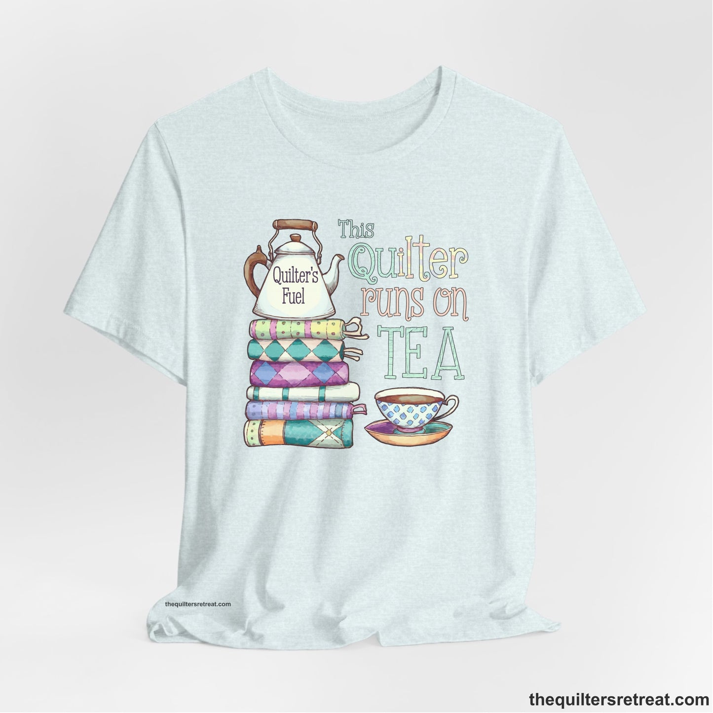 A Heather Ice Blue Short Sleeve T-Shirt with a stack of colorful quilts with teapot and cup, whimsical "This Quilter Runs on Tea" text
