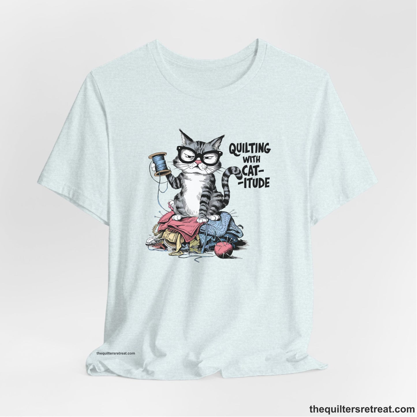 A Heather Ice Blue Short Sleeve T-Shirt with a grumpy cat holding thread spool atop fabric pile with "Quilting with Cat-itude" text