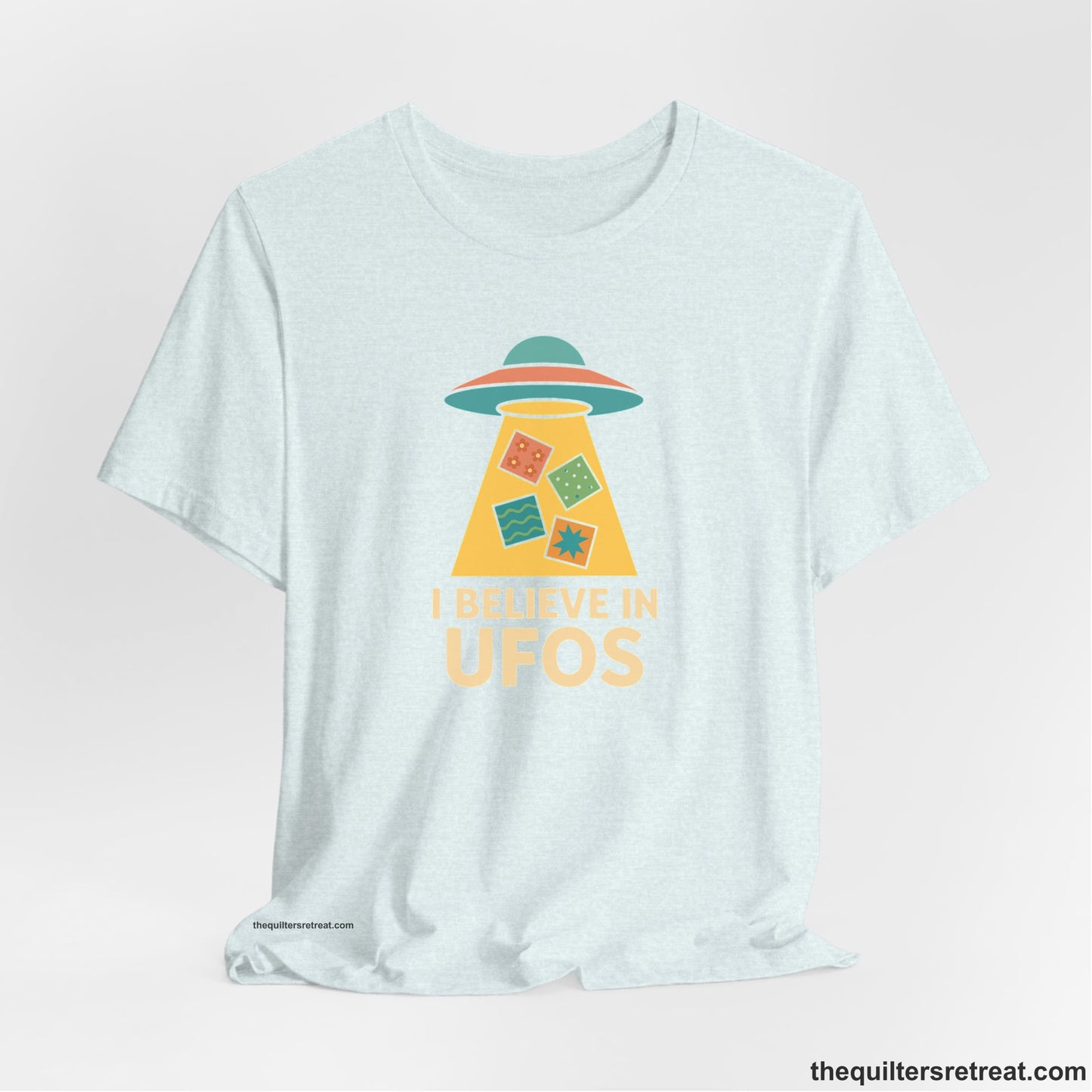 A Heather Ice Blue Short Sleeve T-Shirt with a colorful UFO with quilt patterns and bold "I Believe in UFOs" text in retro style
