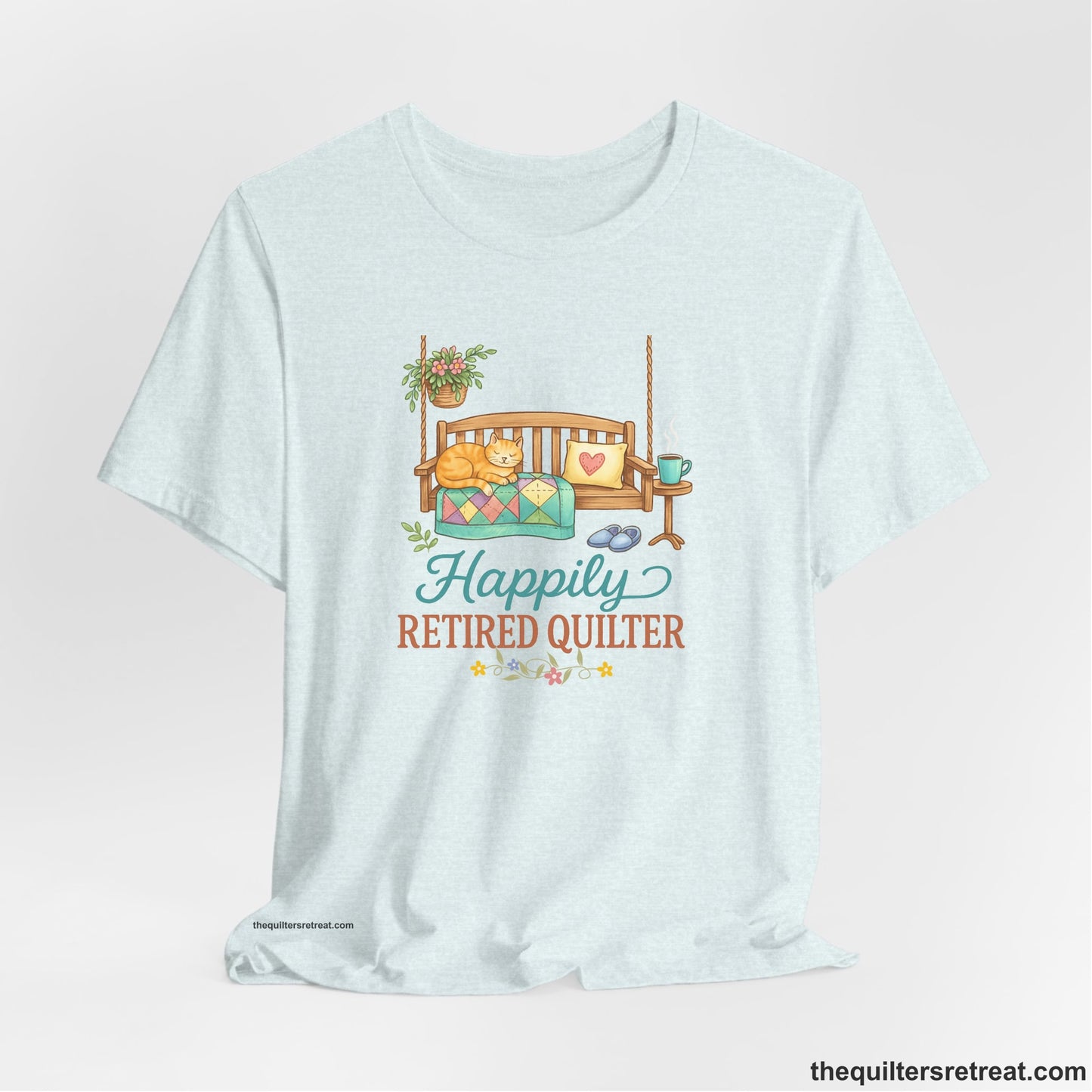A Heather Ice Blue Short Sleeve T-Shirt with a hanging bench with cozy cat and quilt, surrounded by plants, "Happily Retired Quilter" text