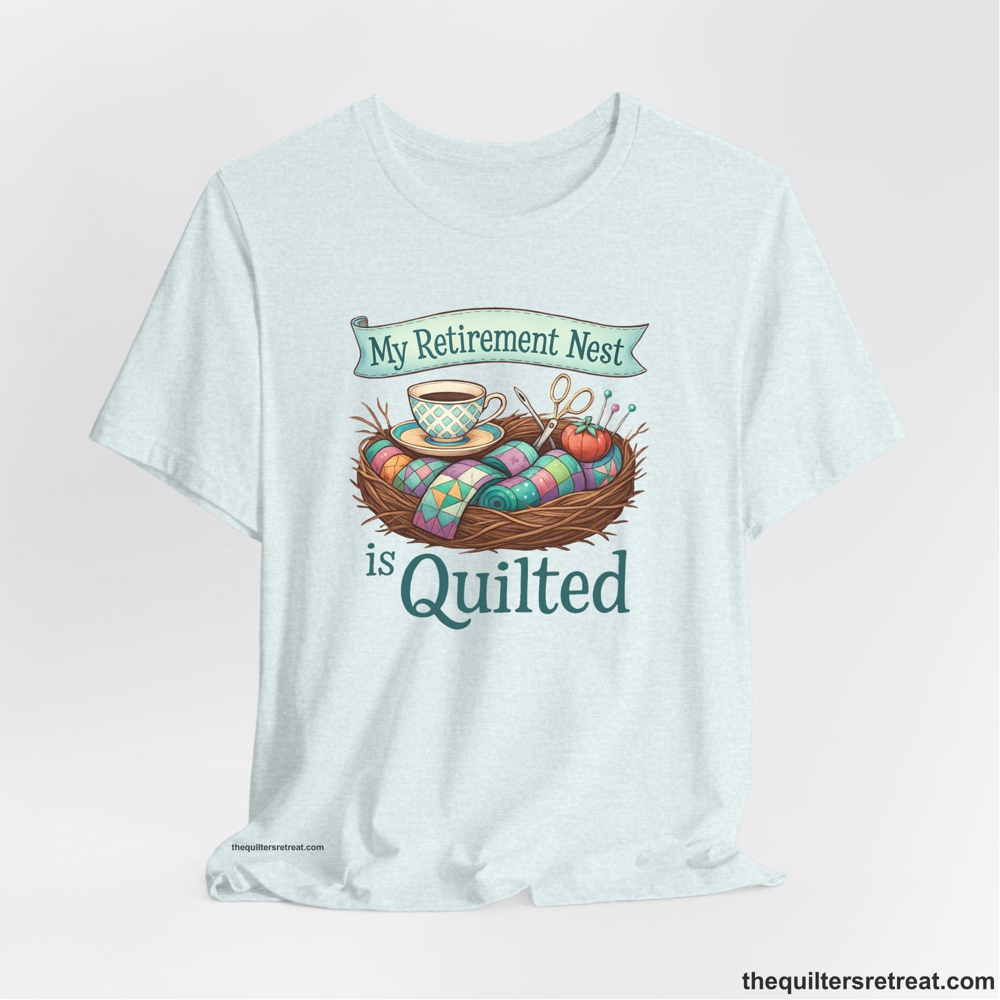 A Heather Ice Blue Short Sleeve T-Shirt with a My Retirement Nest is Quilted text with a cozy sewing elements illustration