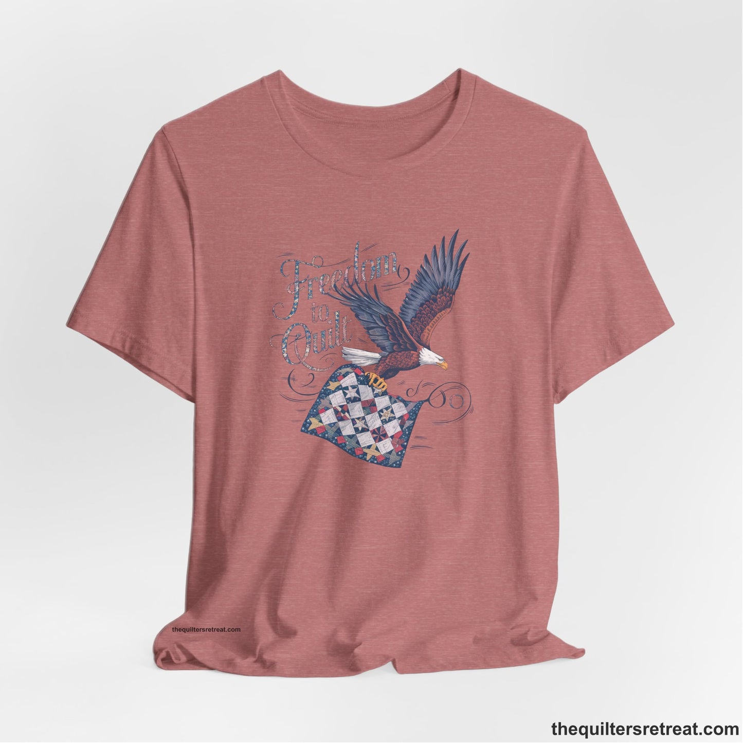 A Heather Mauve Short Sleeve T-Shirt with a freedom to quilt text with an eagle carrying a colorful patchwork quilt in vintage style
