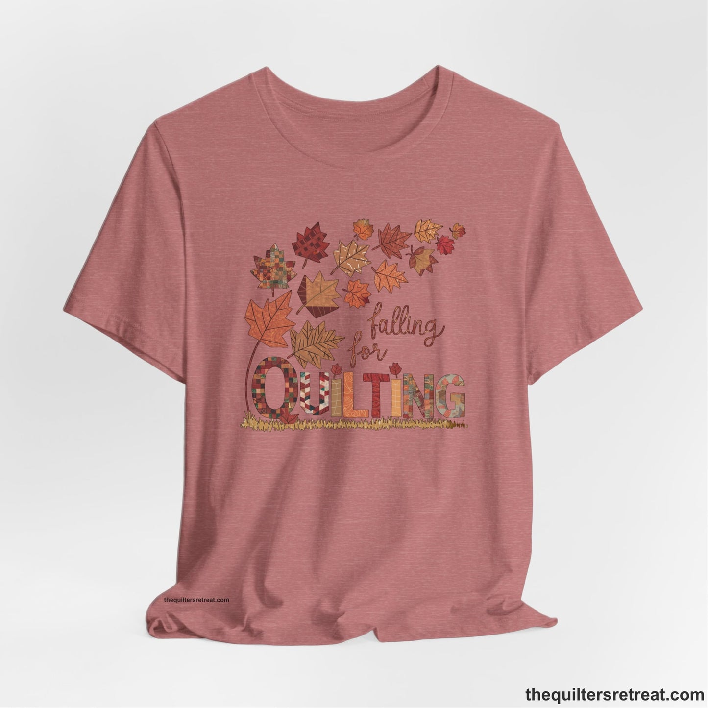 A Heather Mauve Short Sleeve T-Shirt with a falling autumn leaves and "Falling for Quilting" text in a patchwork style