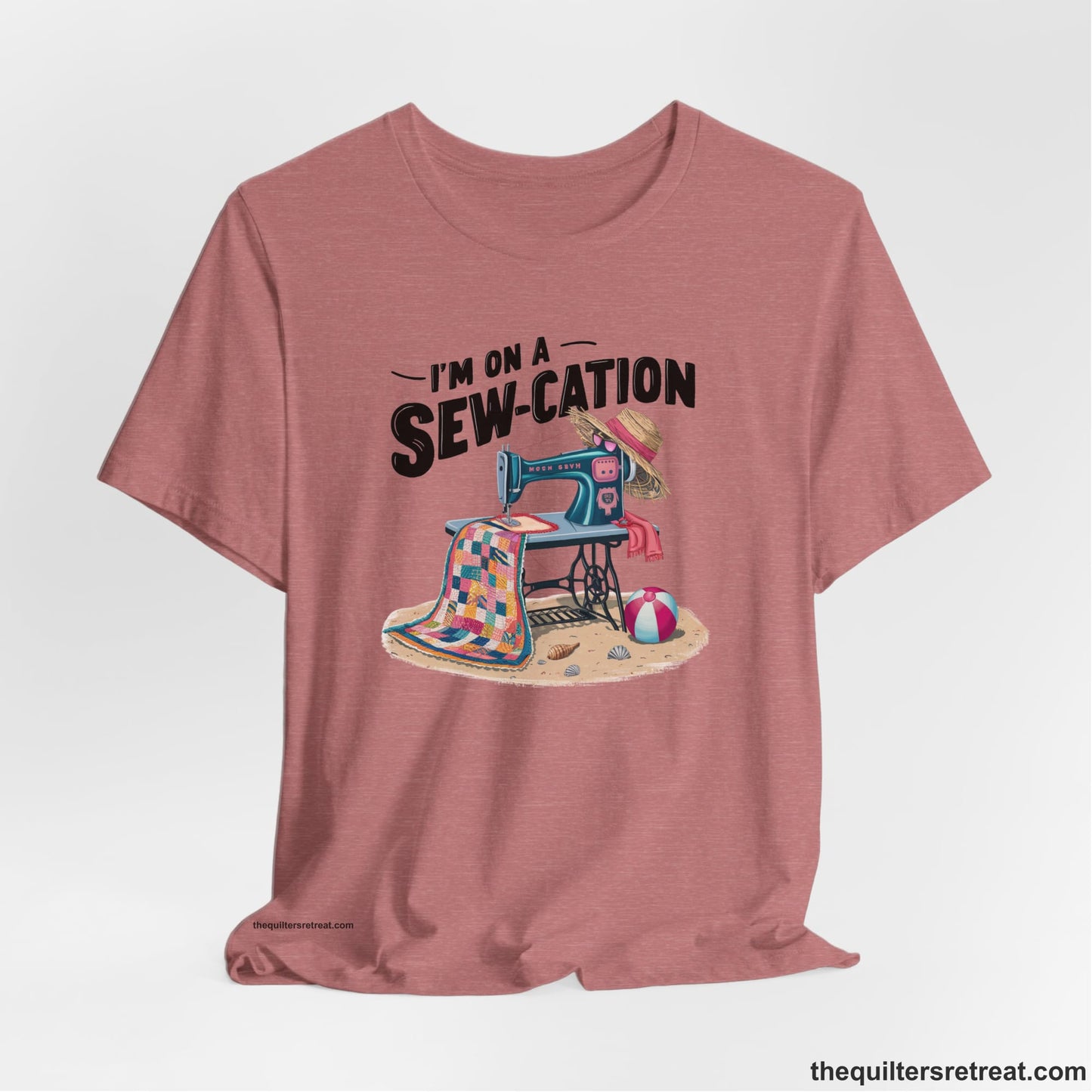 A Heather Mauve Short Sleeve T-Shirt with a vintage sewing machine with colorful quilt, beach items, and "I'm On A Sew-Cation" text