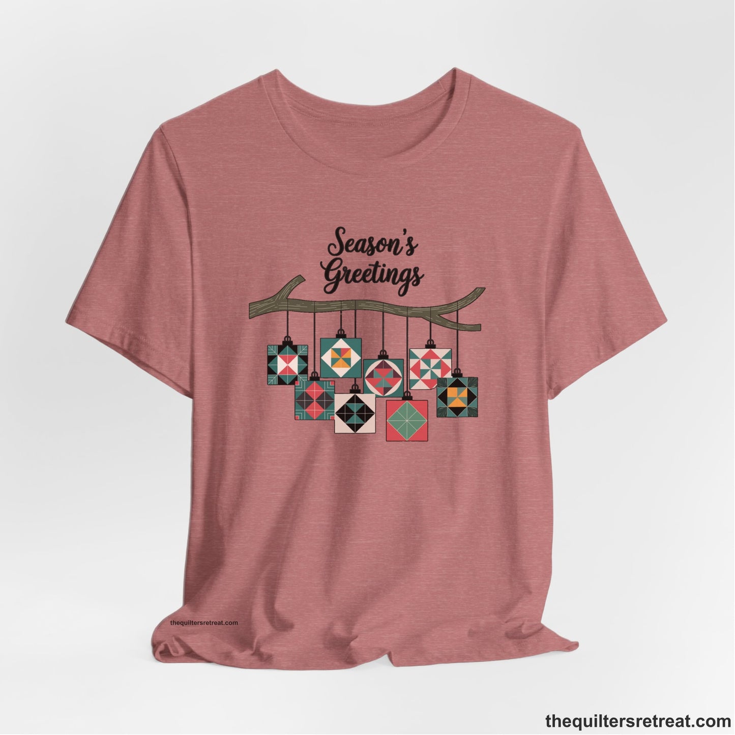 A Heather Mauve Short Sleeve T-Shirt with a season's greetings text above colorful quilt block ornaments on tree branch in rustic style