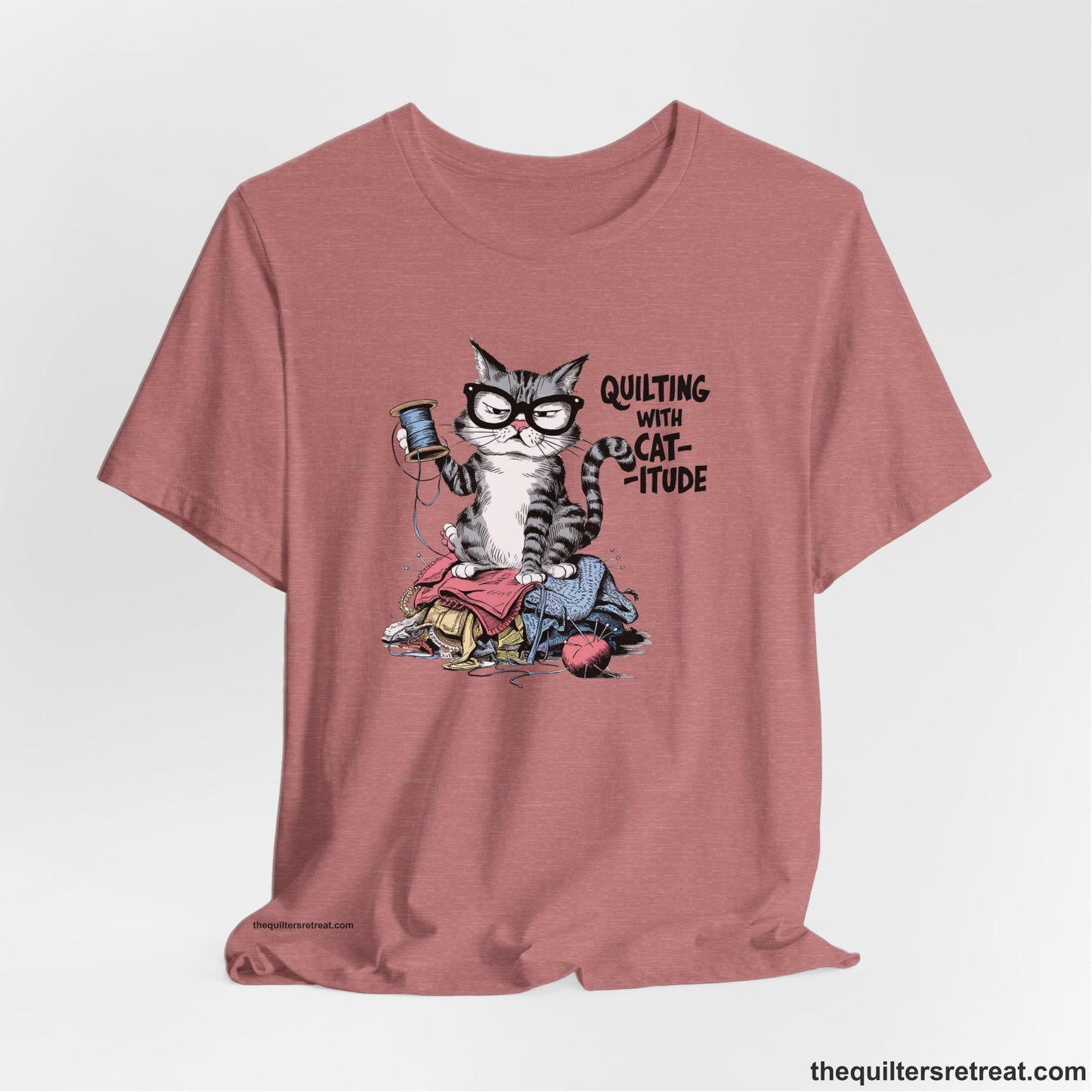 A Heather Mauve Short Sleeve T-Shirt with a grumpy cat holding thread spool atop fabric pile with "Quilting with Cat-itude" text