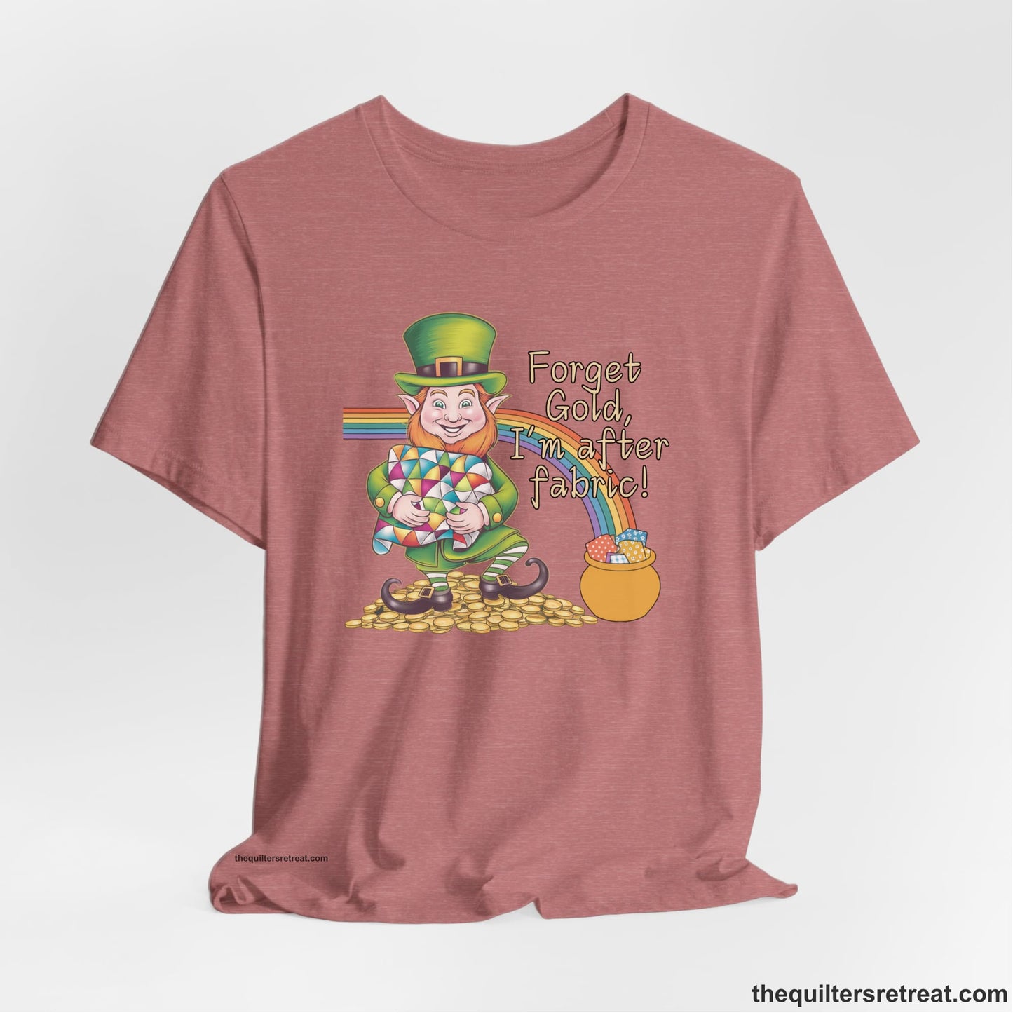 A Heather Mauve Short Sleeve T-Shirt with a leprechaun with colorful quilt and rainbow, whimsical "Forget Gold, I'm after fabric!" text