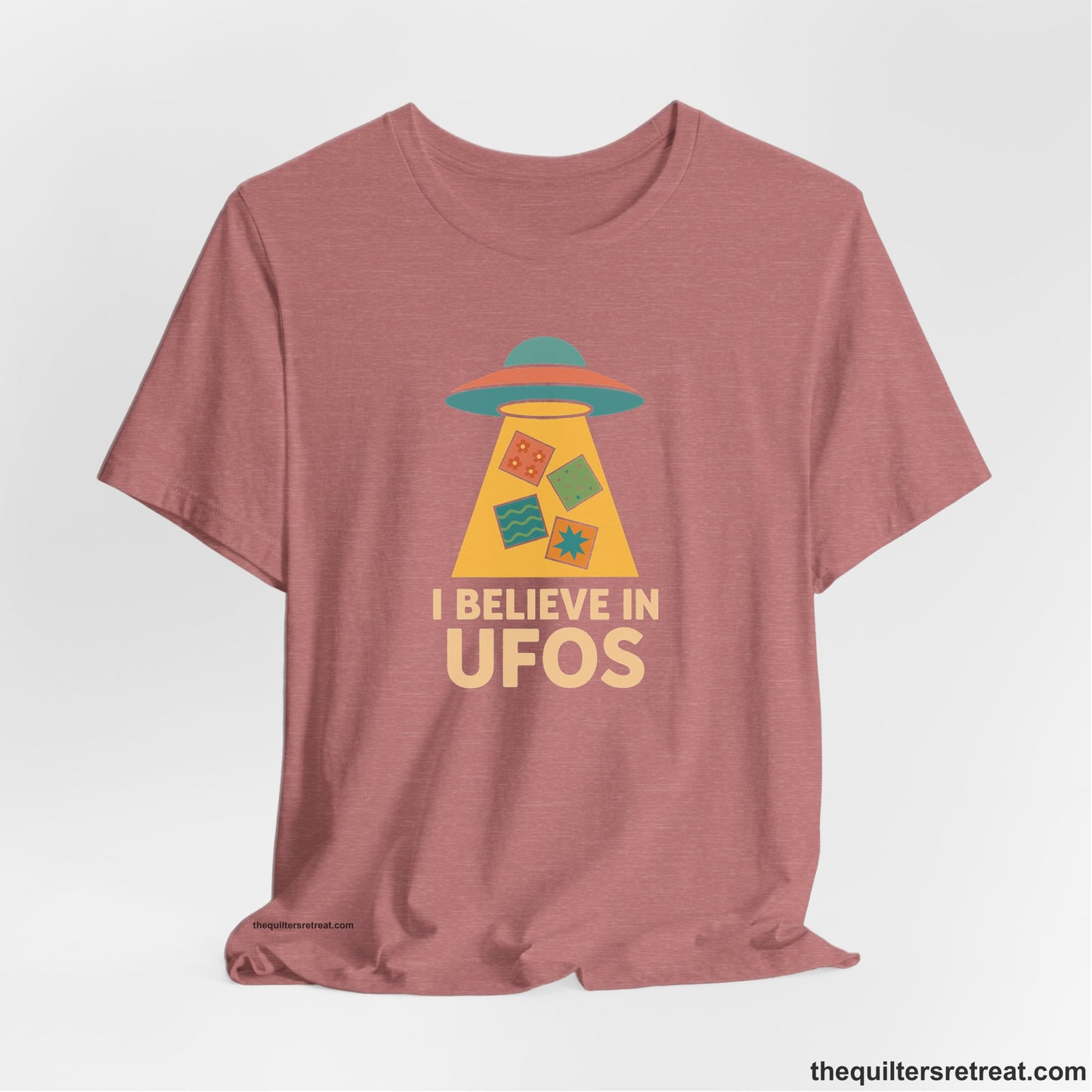 A Heather Mauve Short Sleeve T-Shirt with a colorful UFO with quilt patterns and bold "I Believe in UFOs" text in retro style