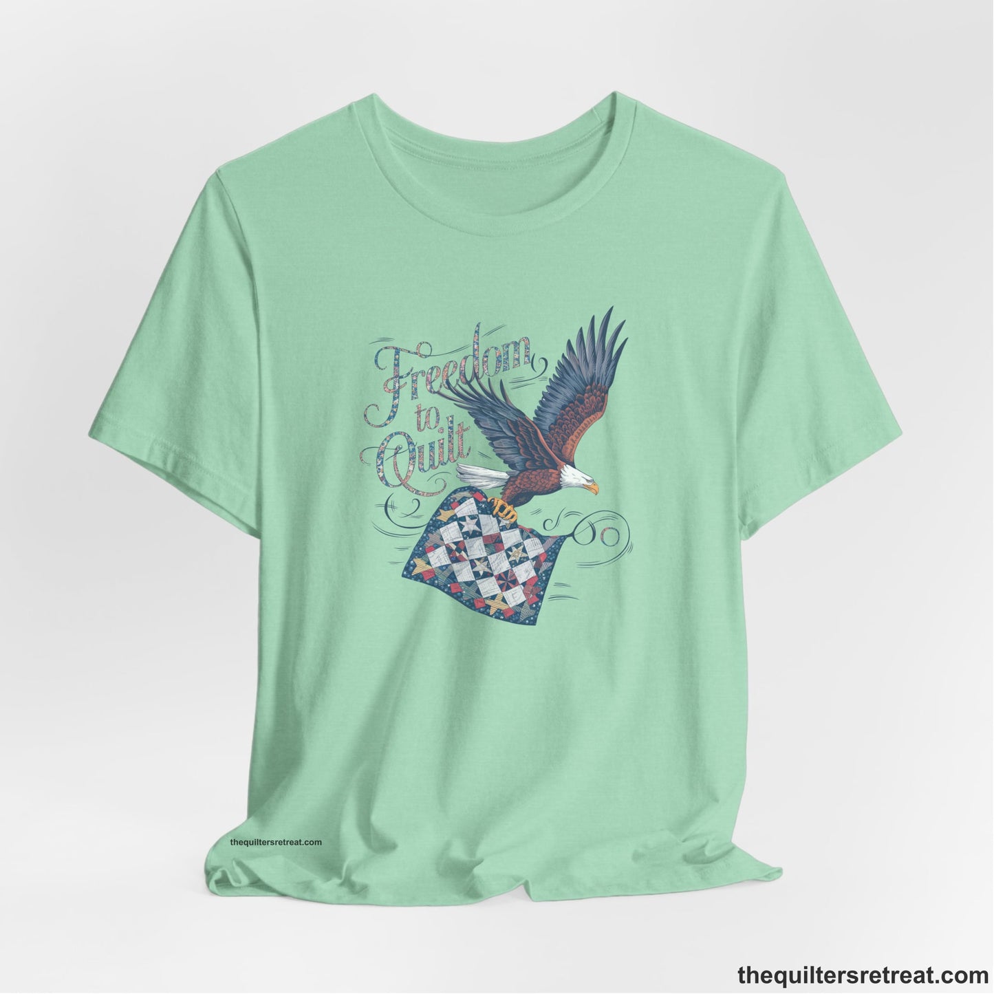 A Heather Mint Short Sleeve T-Shirt with a freedom to quilt text with an eagle carrying a colorful patchwork quilt in vintage style