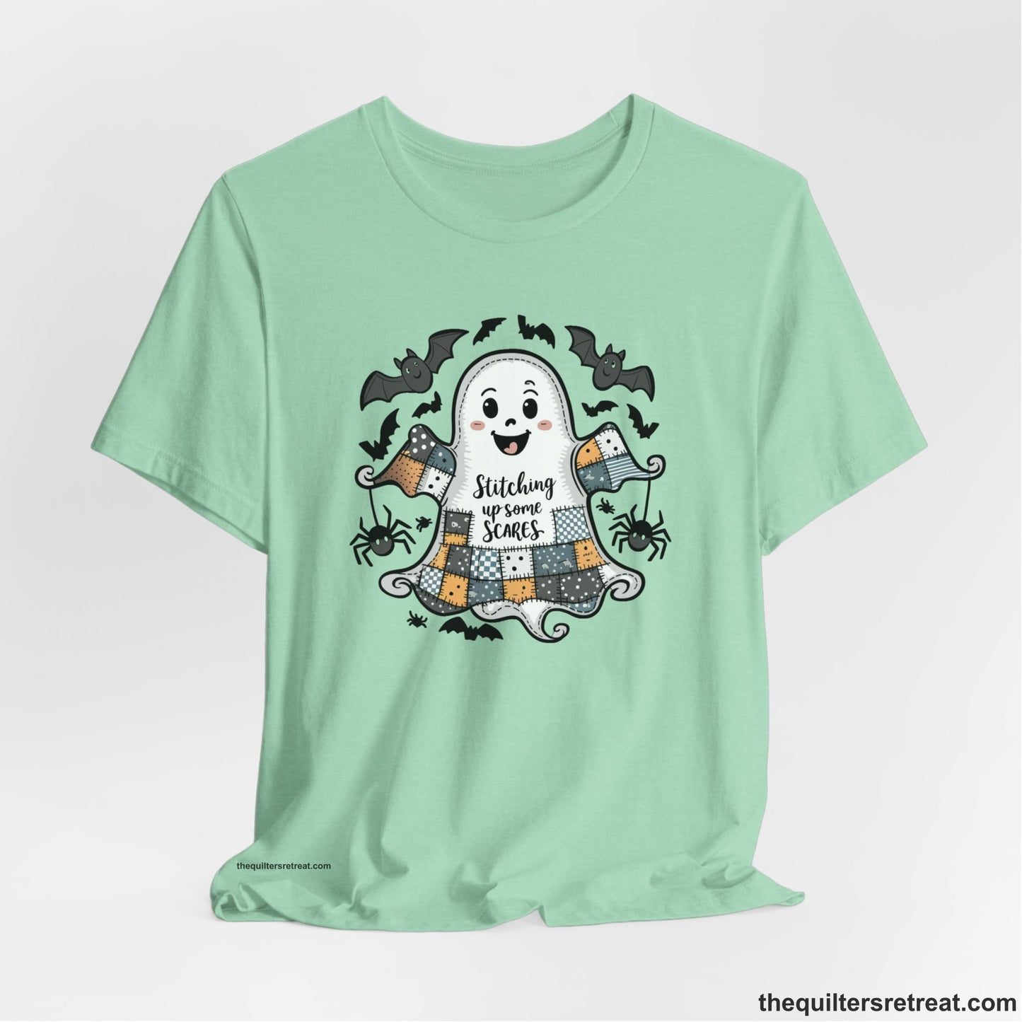 A Heather Mint Short Sleeve T-Shirt with a cute patchwork ghost with "Stitching up some Scares" text and playful bats in a whimsical style