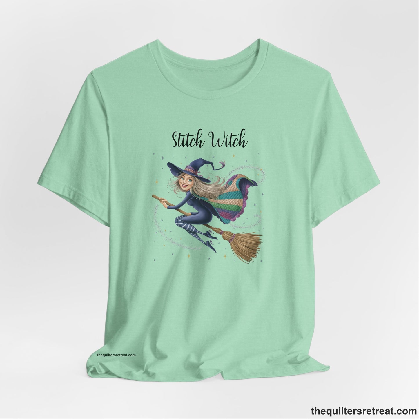 A Heather Mint Short Sleeve T-Shirt with a playful witch on broomstick with patchwork cape and starry background in a whimsical style