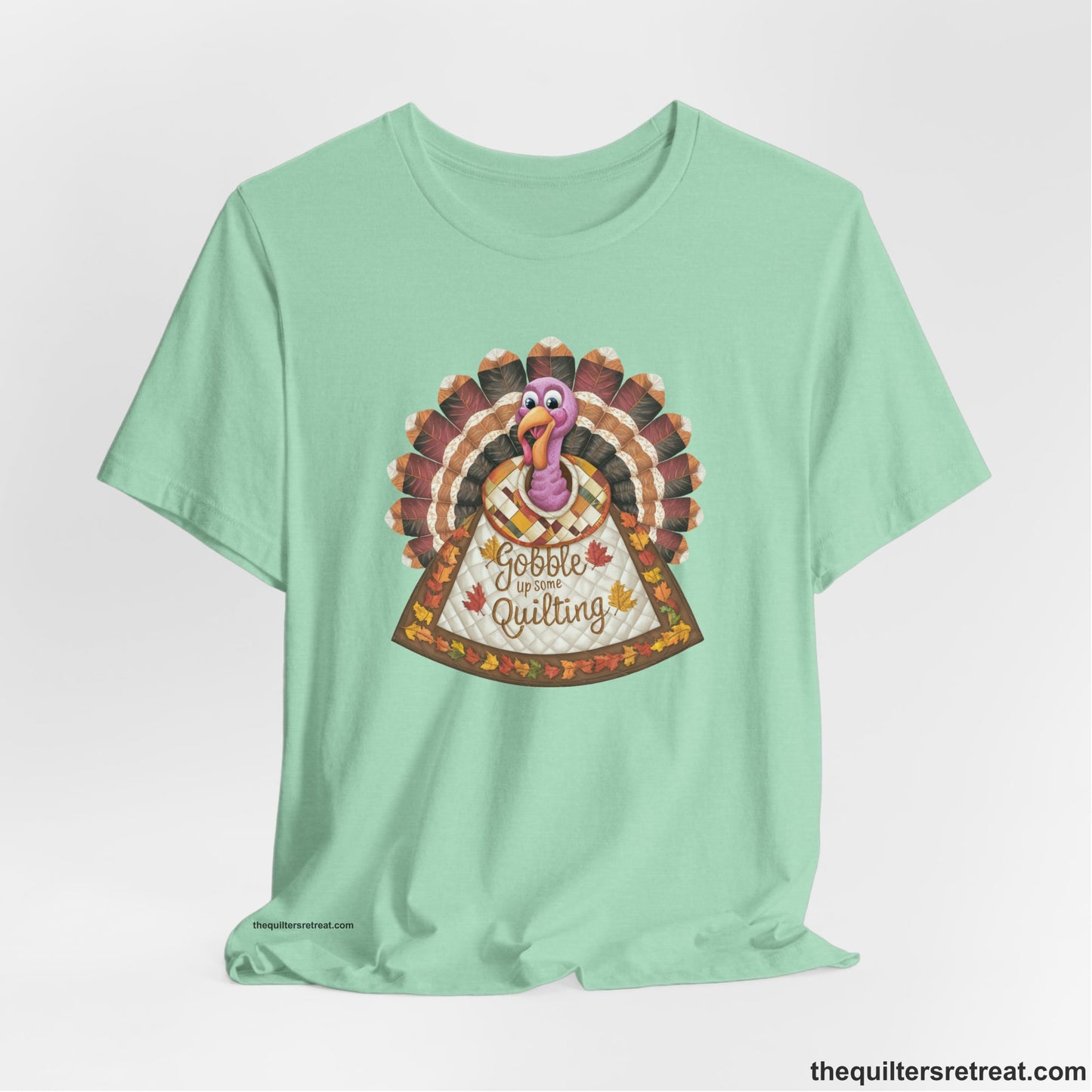 A Heather Mint Short Sleeve T-Shirt with a colorful turkey with quilted feathers and "Gobble Up Some Quilting" text in a playful style