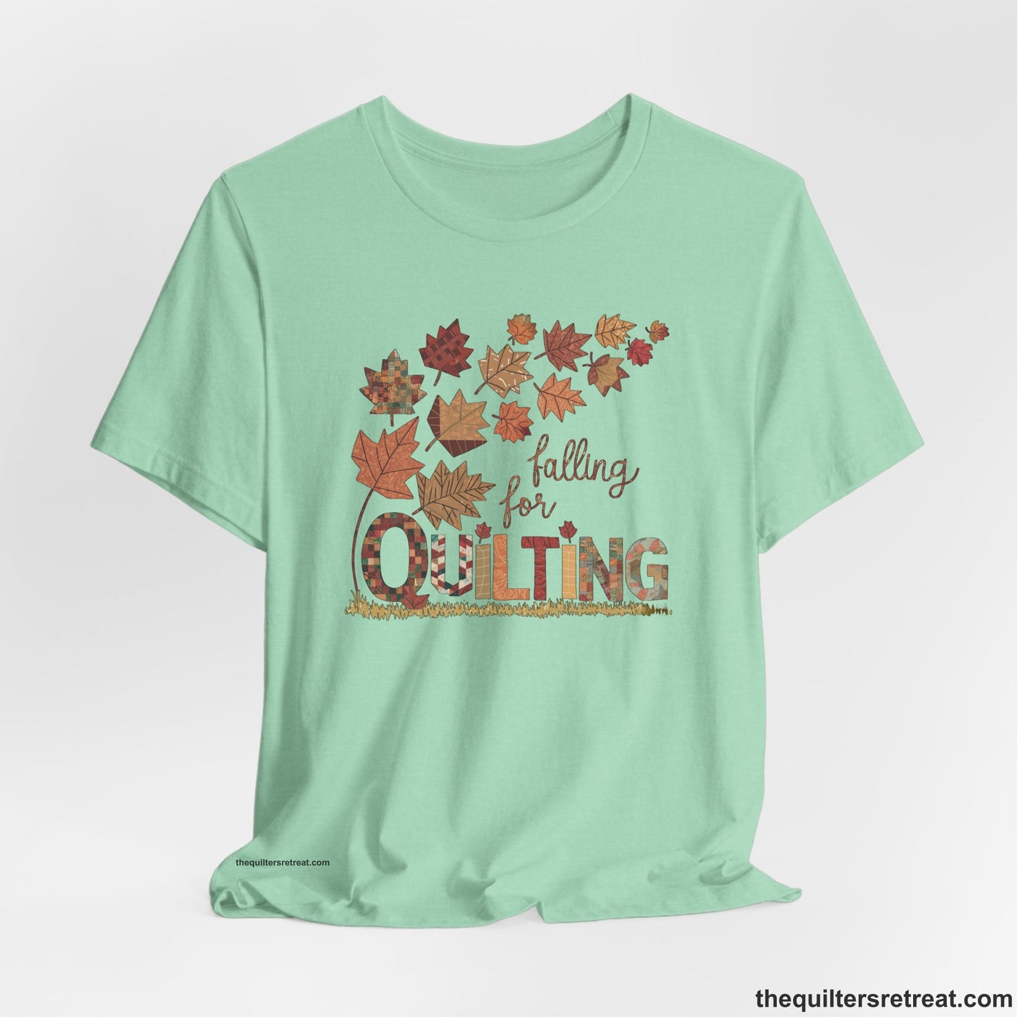A Heather Mint Short Sleeve T-Shirt with a falling autumn leaves and "Falling for Quilting" text in a patchwork style