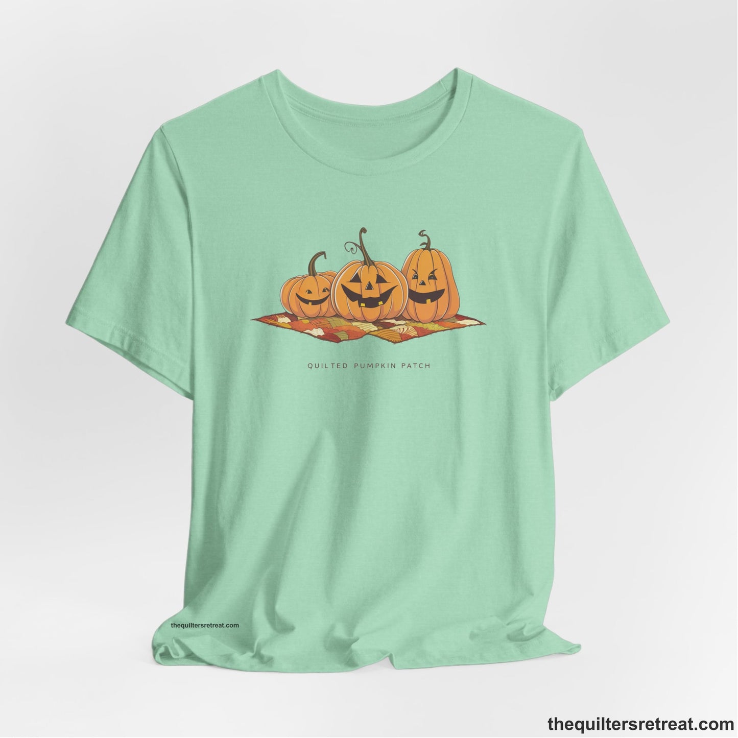A Heather Mint Short Sleeve T-Shirt with a playful jack-o'-lantern trio on a quilt with "Quilted Pumpkin Patch" text