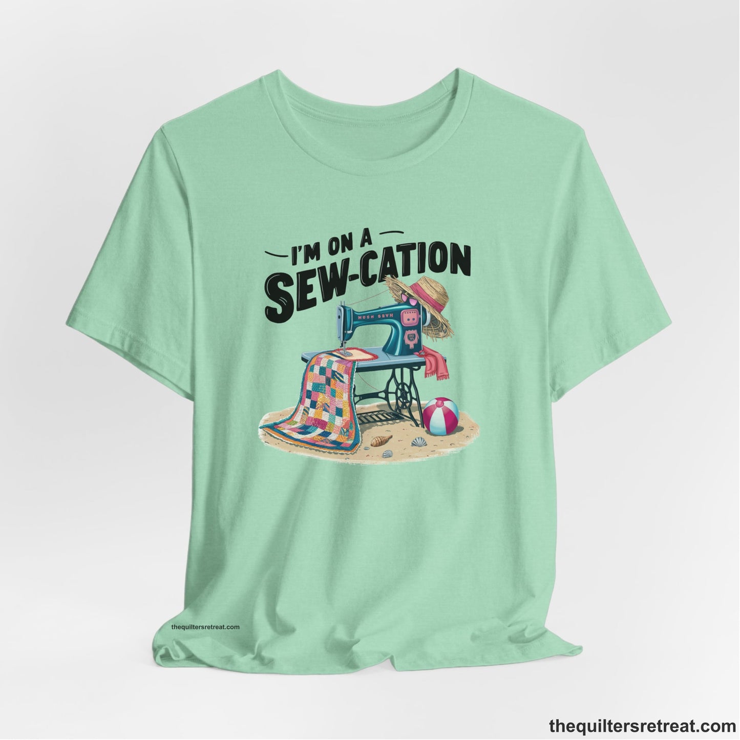 A Heather Mint Short Sleeve T-Shirt with a vintage sewing machine with colorful quilt, beach items, and "I'm On A Sew-Cation" text