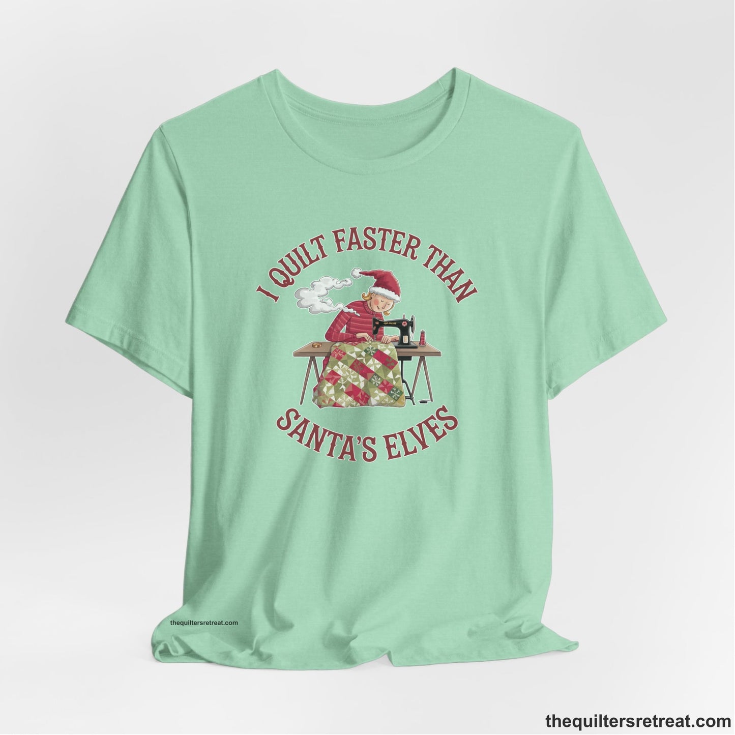 A Heather Mint Short Sleeve T-Shirt with a whimsical illustration of a quilting woman with "I Quilt Faster Than Santa's Elves" text