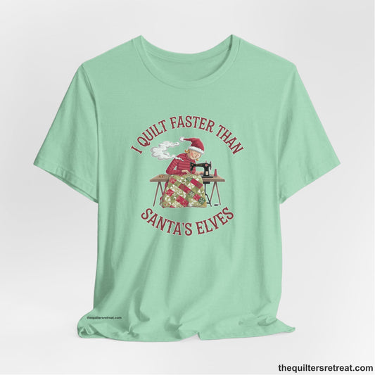 A Heather Mint Short Sleeve T-Shirt with a whimsical illustration of a quilting woman with "I Quilt Faster Than Santa's Elves" text