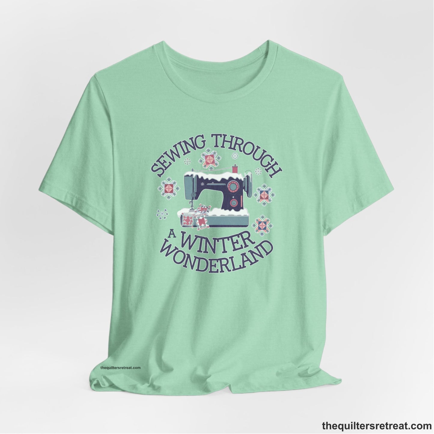 A Heather Mint Short Sleeve T-Shirt with a sewing machine covered in snow with festive quilting elements and "Sewing Through a Winter Wonderland" text