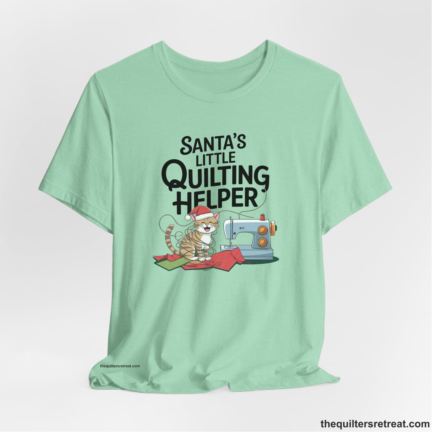 A Heather Mint Short Sleeve T-Shirt with a santa-hat-wearing kitten with a sewing machine and "Santa's Little Quilting Helper" text in playful style