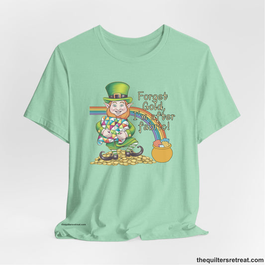 A Heather Mint Short Sleeve T-Shirt with a leprechaun with colorful quilt and rainbow, whimsical "Forget Gold, I'm after fabric!" text