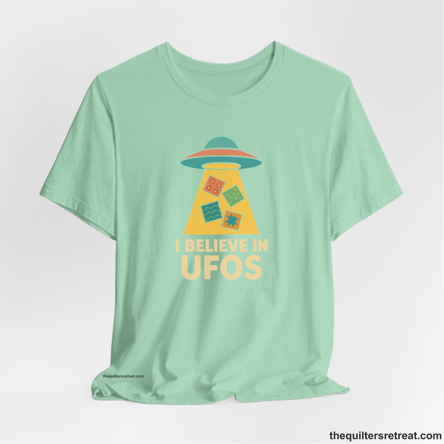 A Heather Mint Short Sleeve T-Shirt with a colorful UFO with quilt patterns and bold "I Believe in UFOs" text in retro style