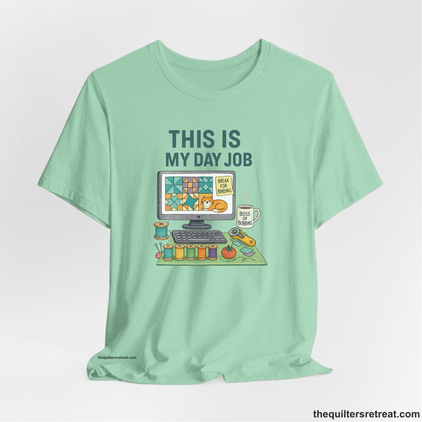 A Heather Mint Short Sleeve T-Shirt with a computer quilt design, cat illustration, "THIS IS MY DAY JOB" text with sewing tools, playful style